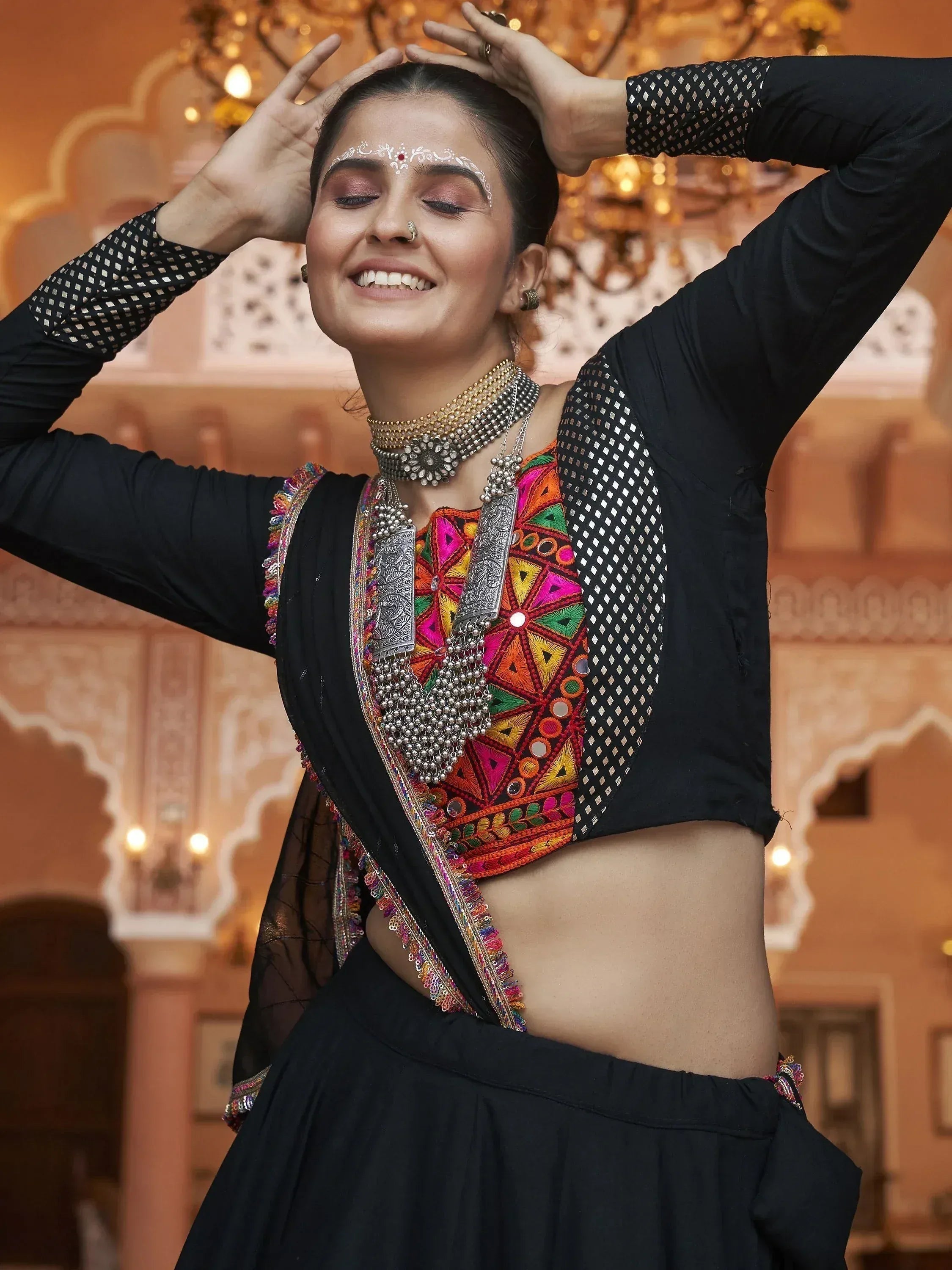 Woman in black ethnic lehenga choli with colorful mirror work and silver jewelry, dancing joyfully