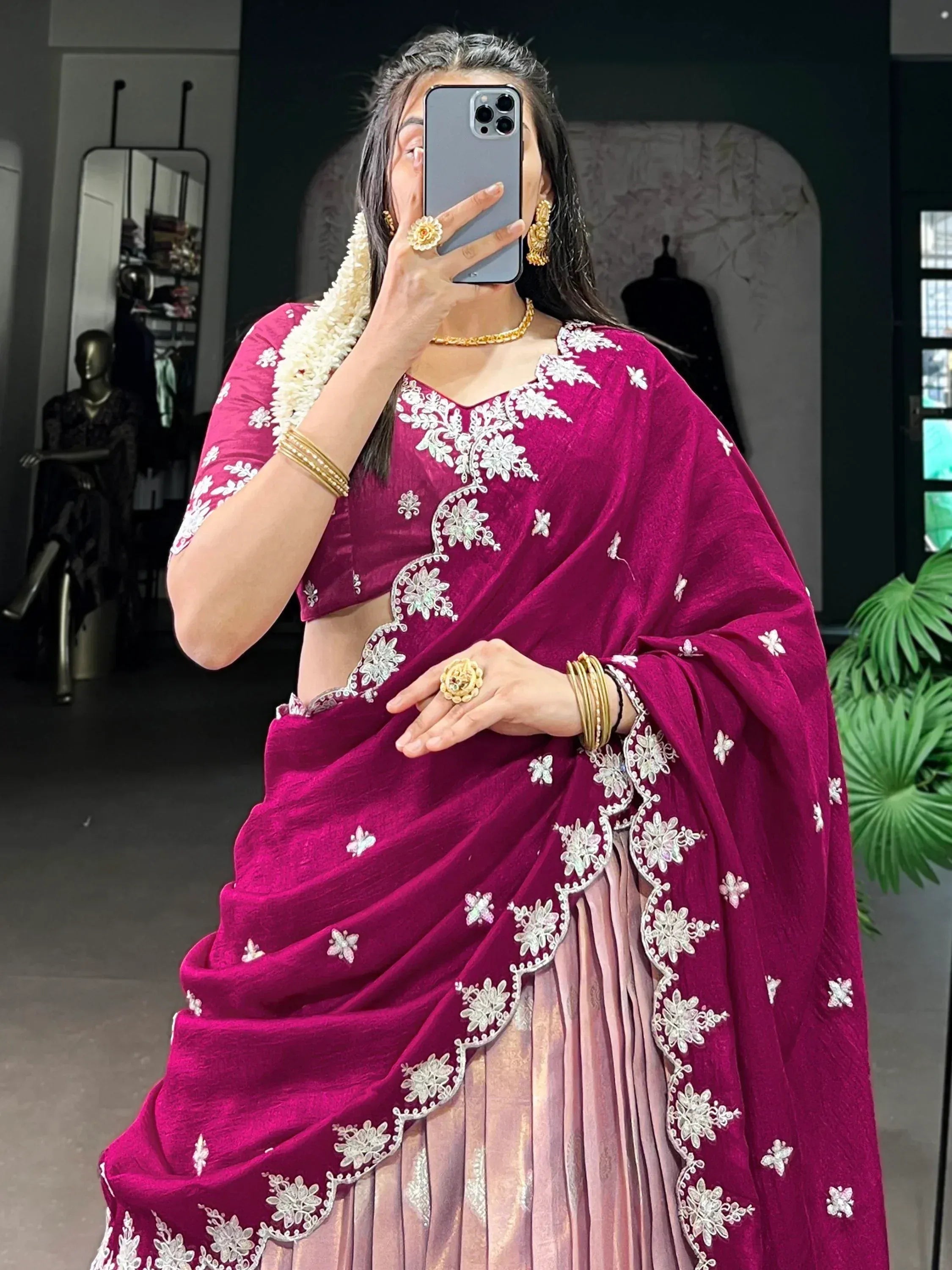 Woman in magenta embroidered lehenga choli with floral detailing, gold jewelry, and white flower garland