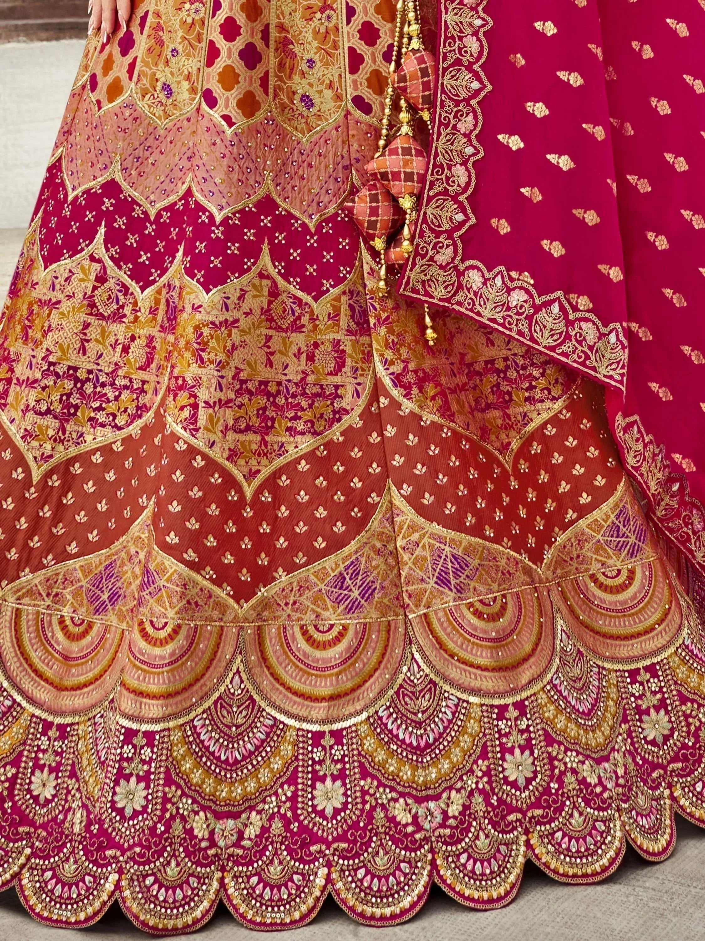 Designer lehenga choli with intricate gold embroidery and vibrant pink-red hues, perfect for Indian weddings.