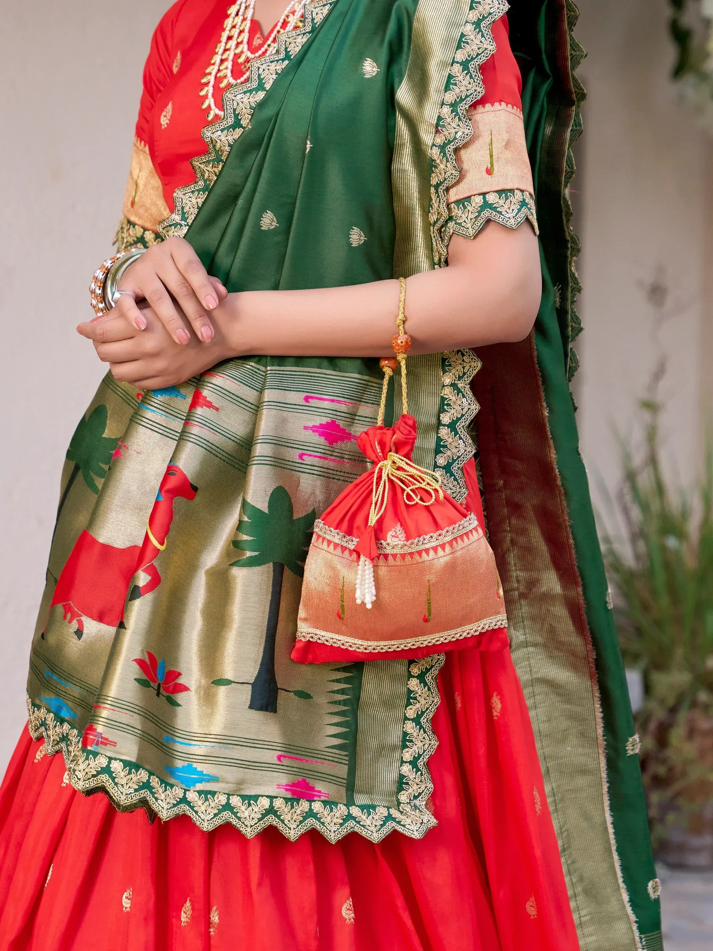 Red and green designer lehenga choli with gold embroidery and matching potli bag, perfect for Indian ethnic wear.