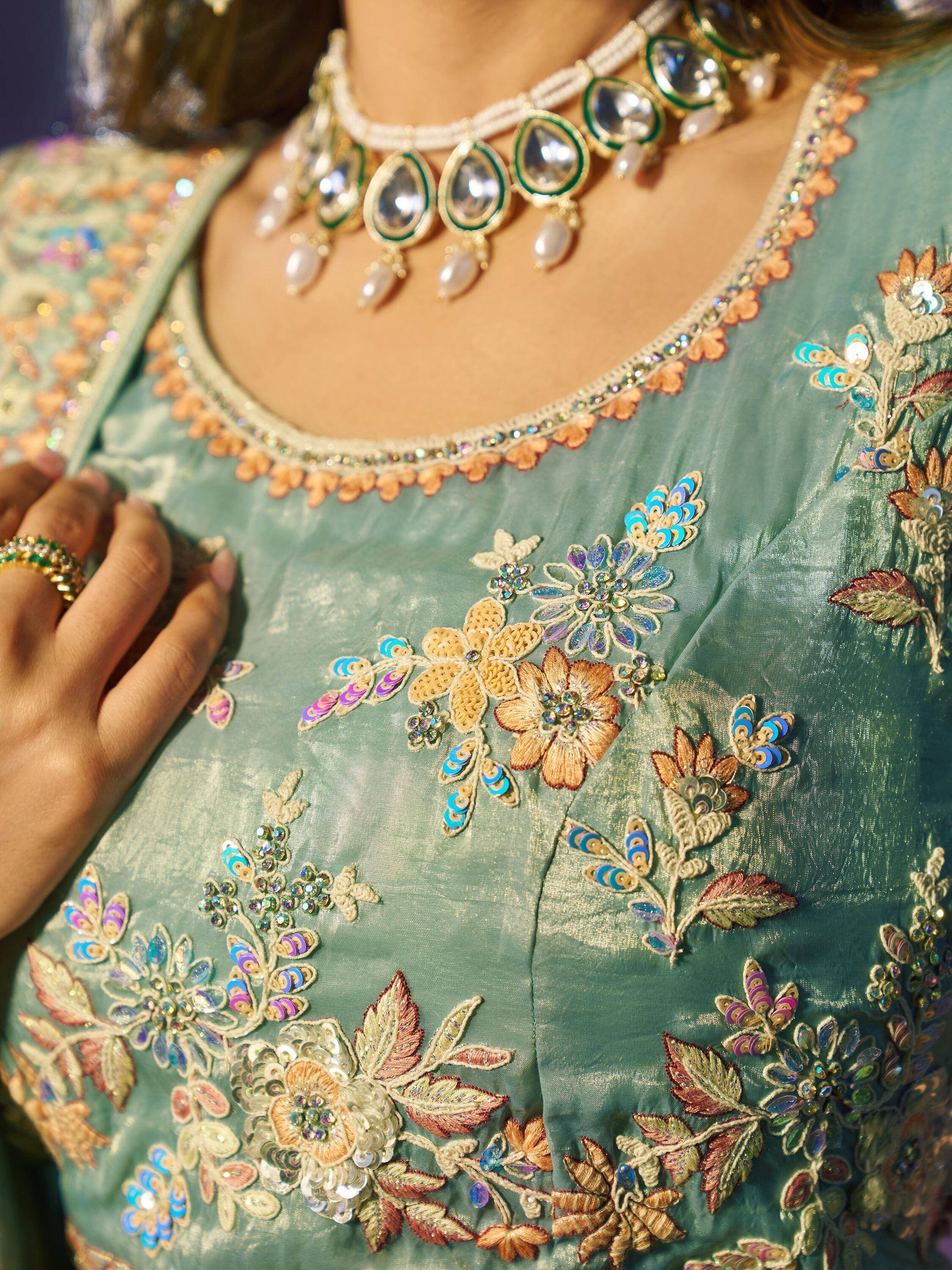 Teal ethnic gown with floral embroidery and pearl necklace, perfect for Indian weddings or festive occasions.