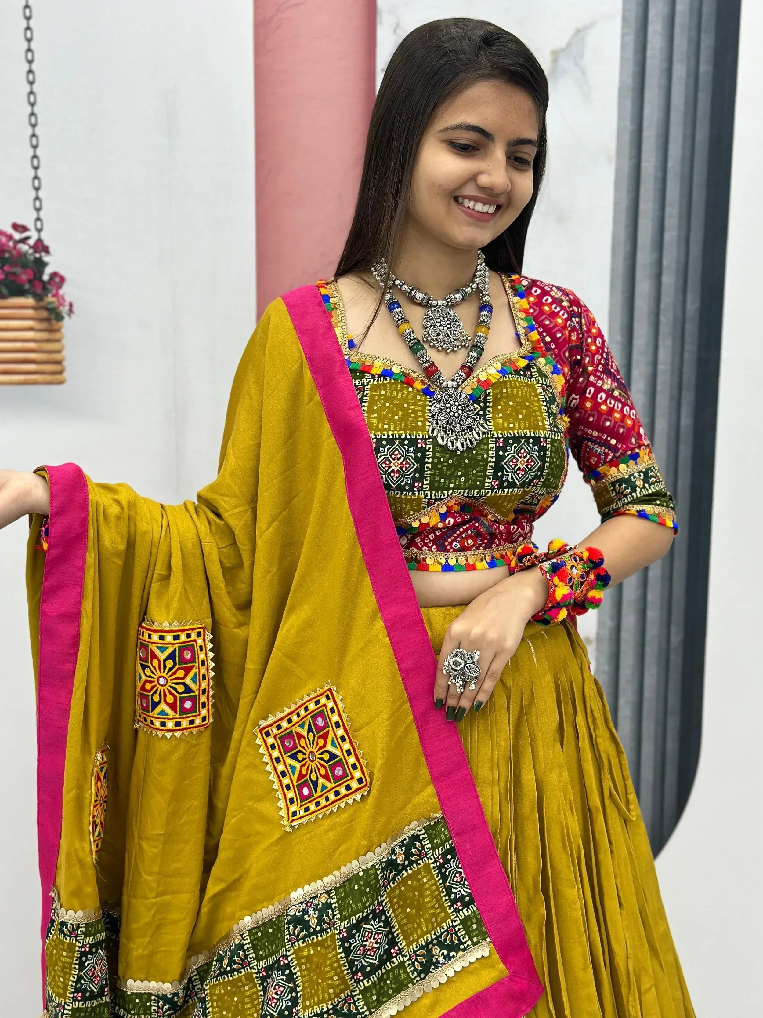 Woman in vibrant yellow ethnic lehenga choli with mirror work, colorful embroidery, and pink dupatta.
