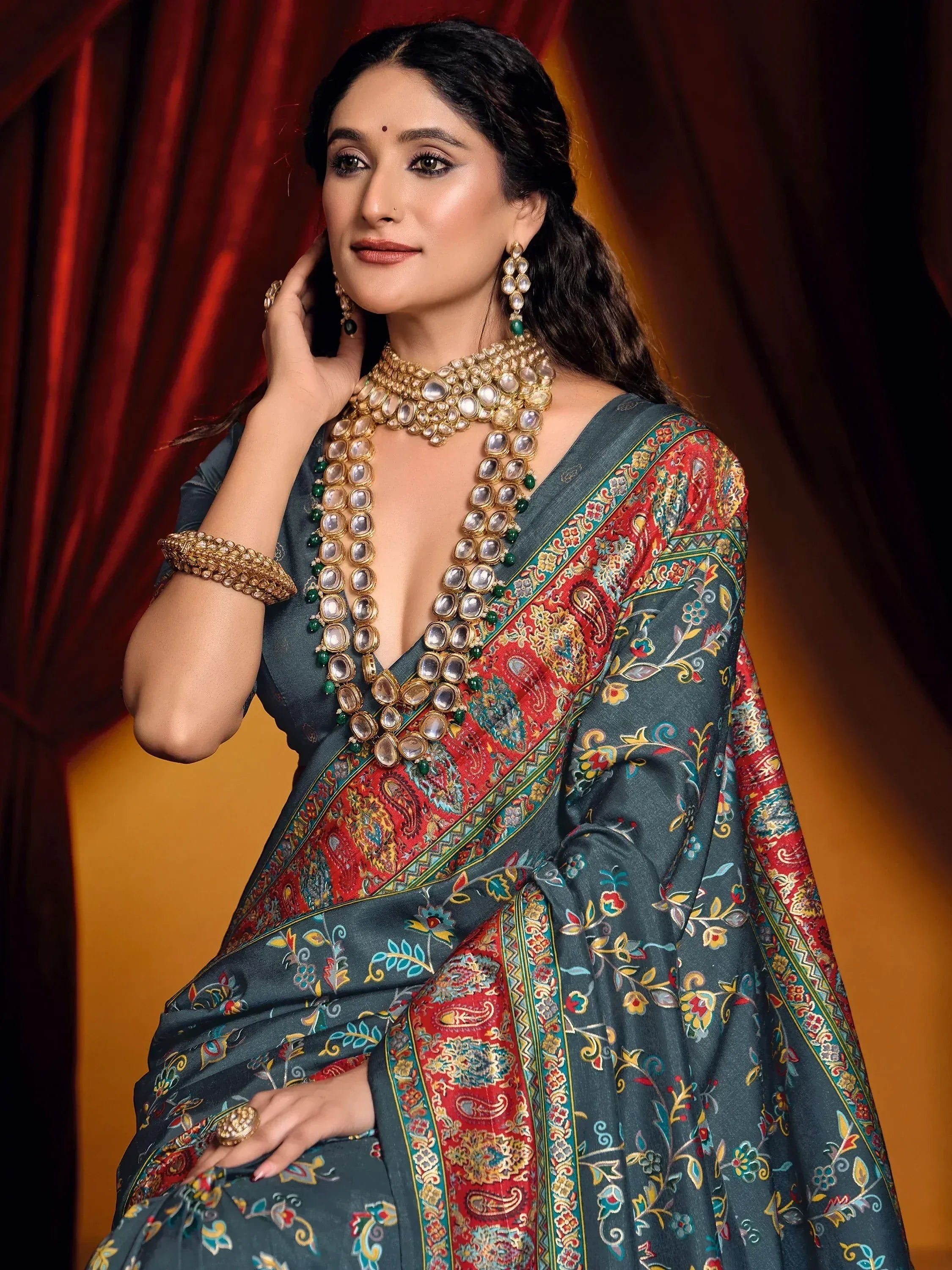 Woman in elegant grey saree with red paisley border, paired with traditional Indian jewelry for festive occasions.