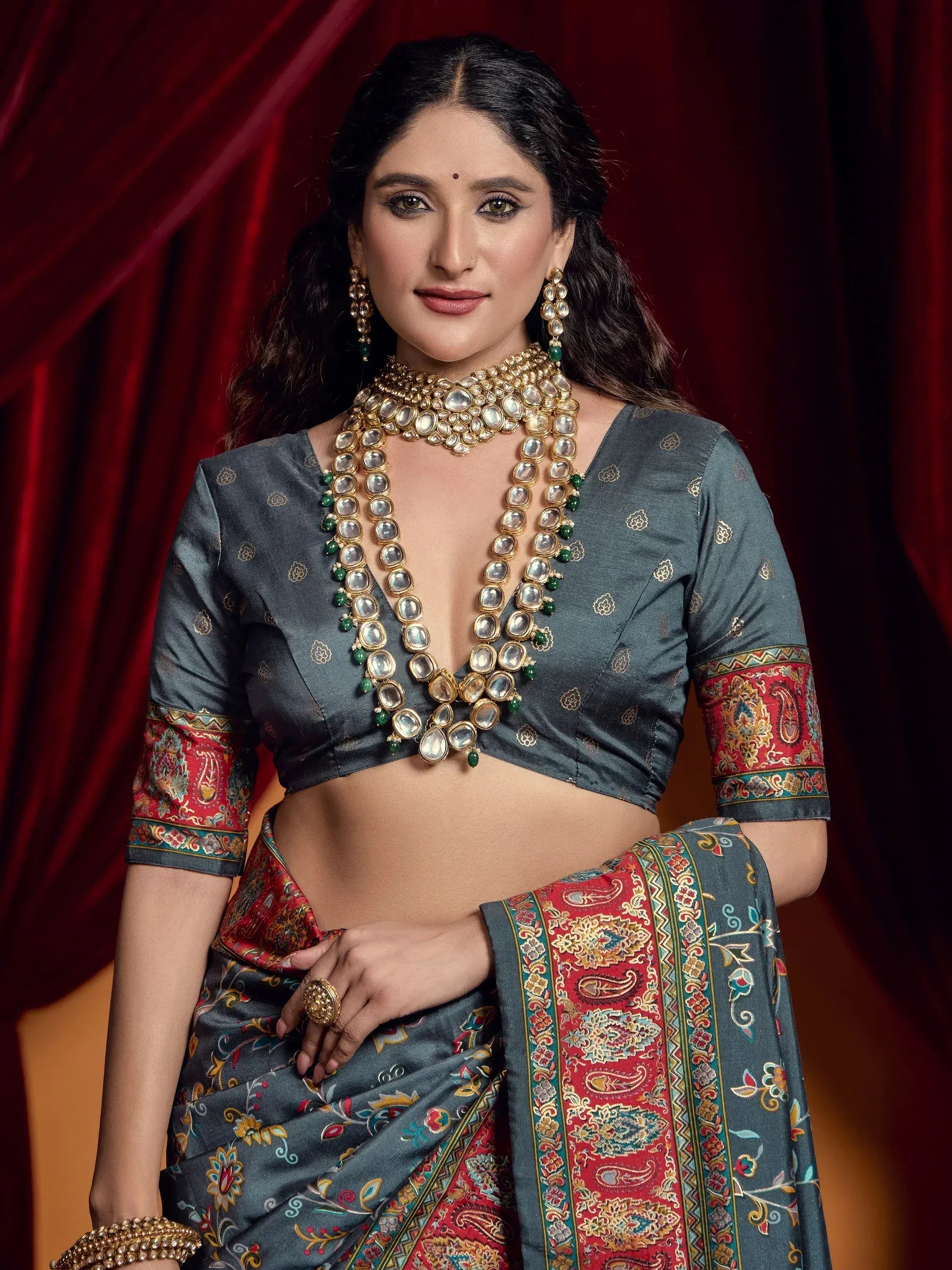 Woman in grey floral saree with red border, gold jewelry, and traditional Indian ethnic wear