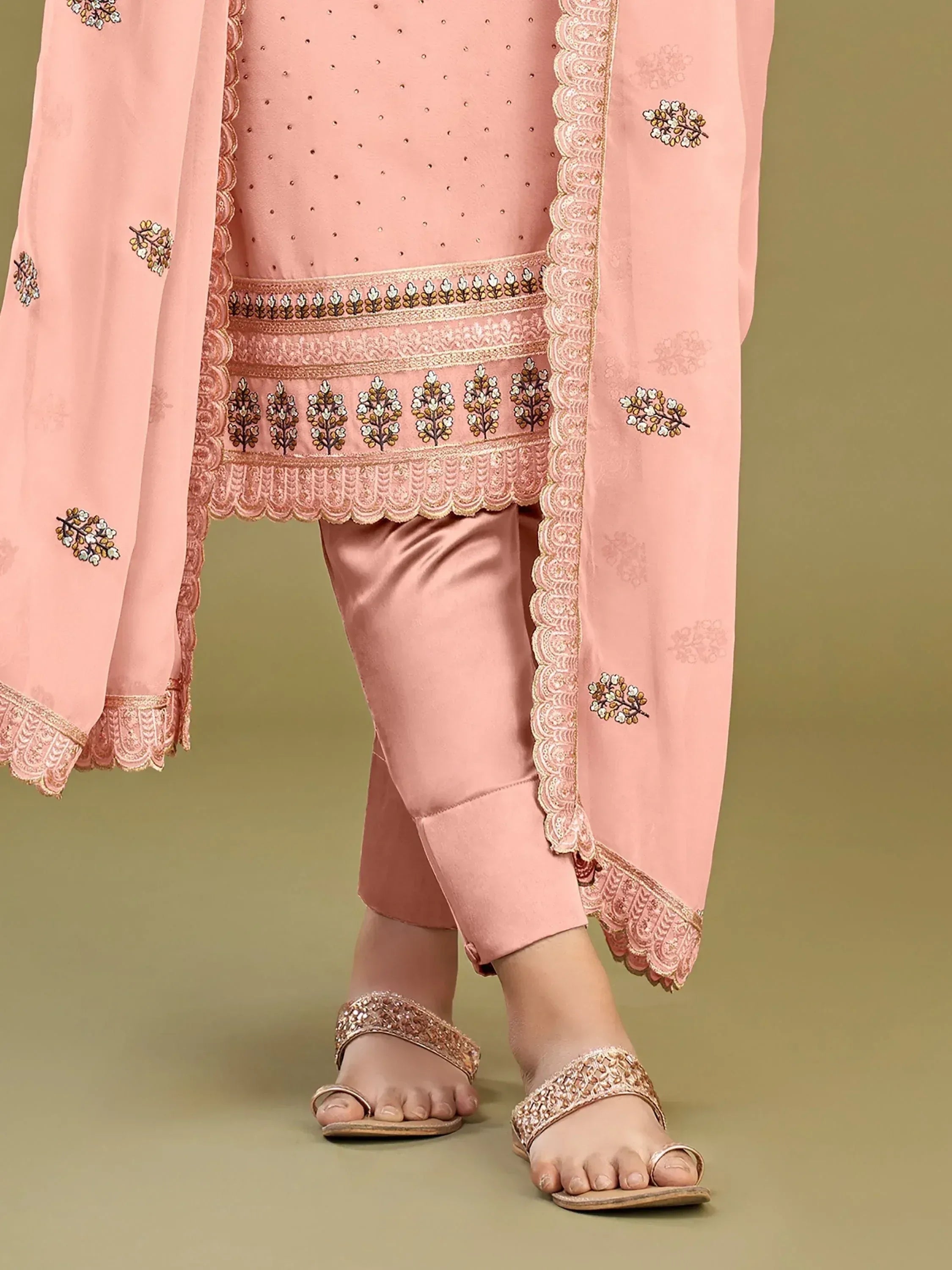 Pink embroidered salwar kameez with floral motifs and scalloped hem, paired with matching pants and embellished sandals