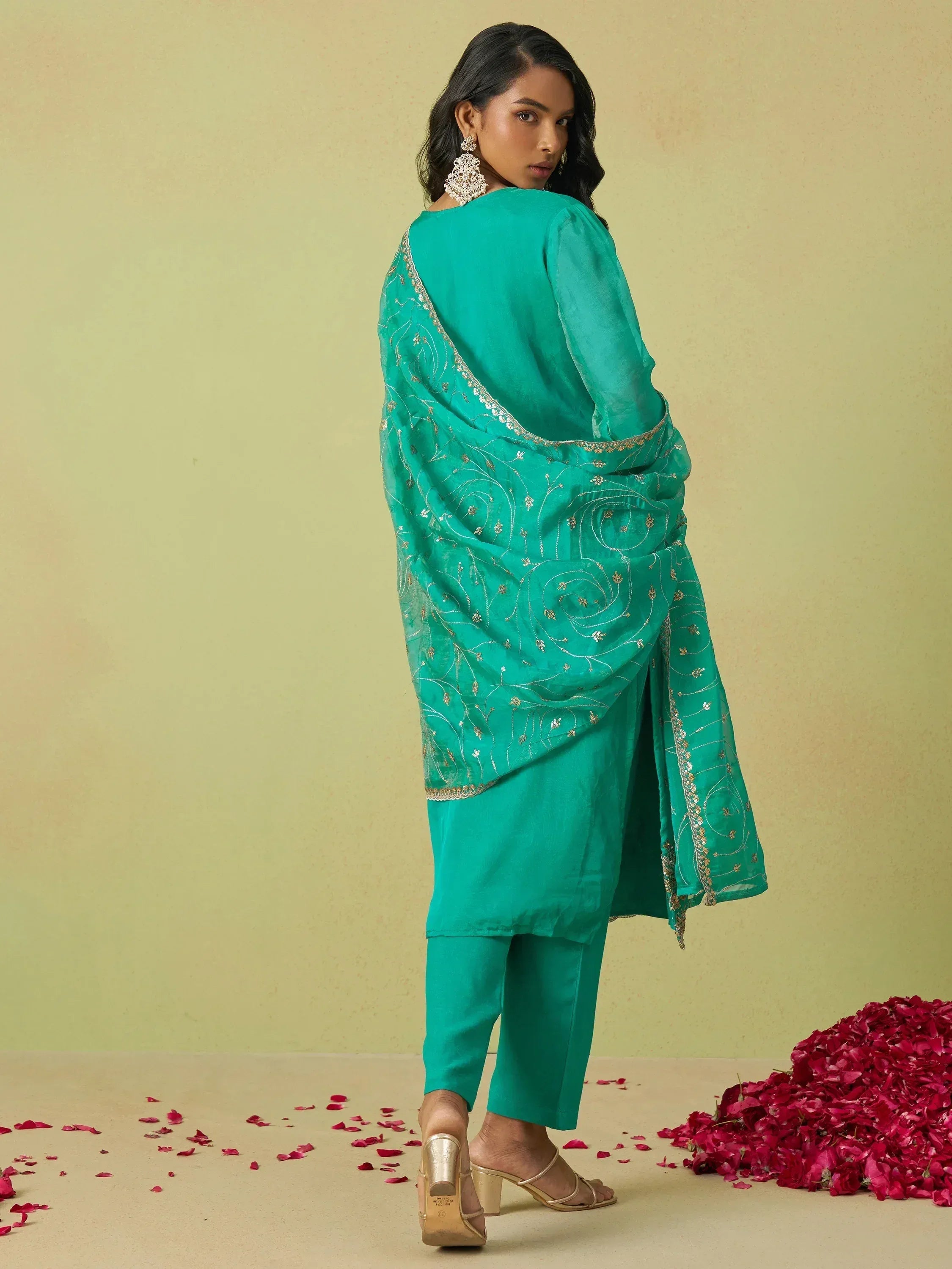 Teal embroidered salwar kameez with gold detailing, paired with elegant heels and rose petals