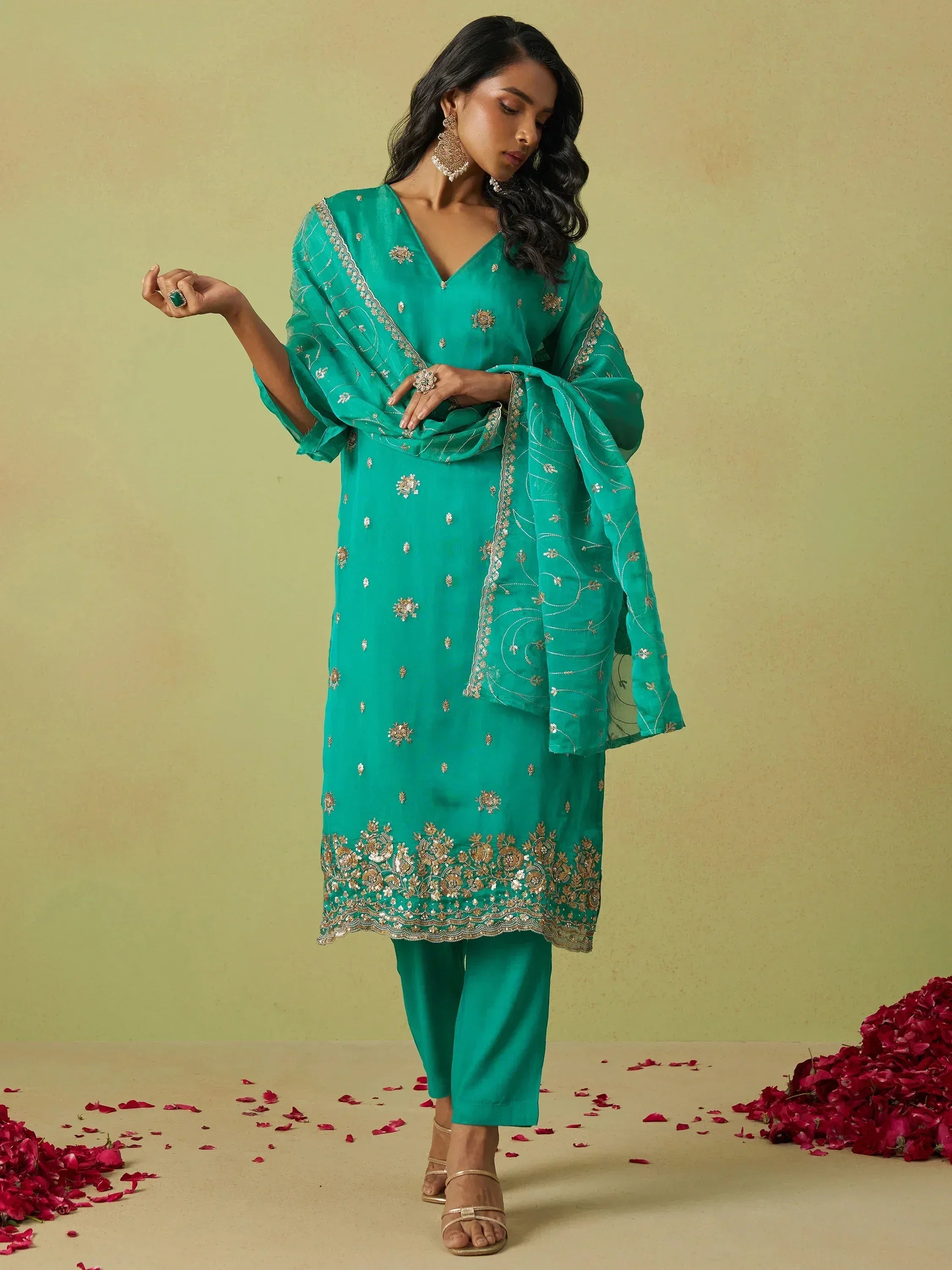 Emerald green embroidered salwar kameez with gold detailing and matching dupatta, styled with rose petals.