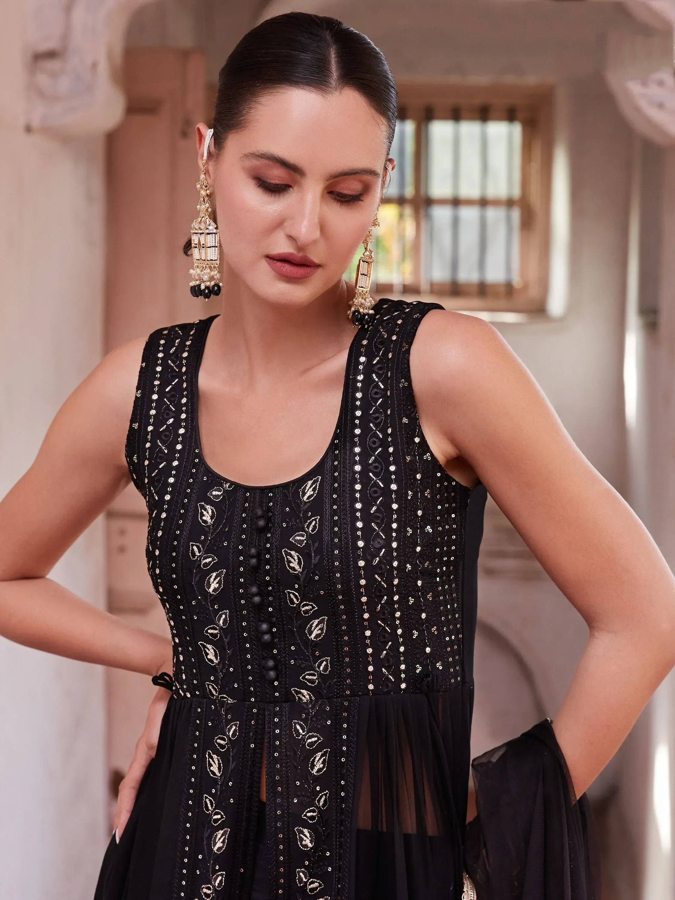 Woman in a black embroidered sleeveless ethnic gown with gold earrings