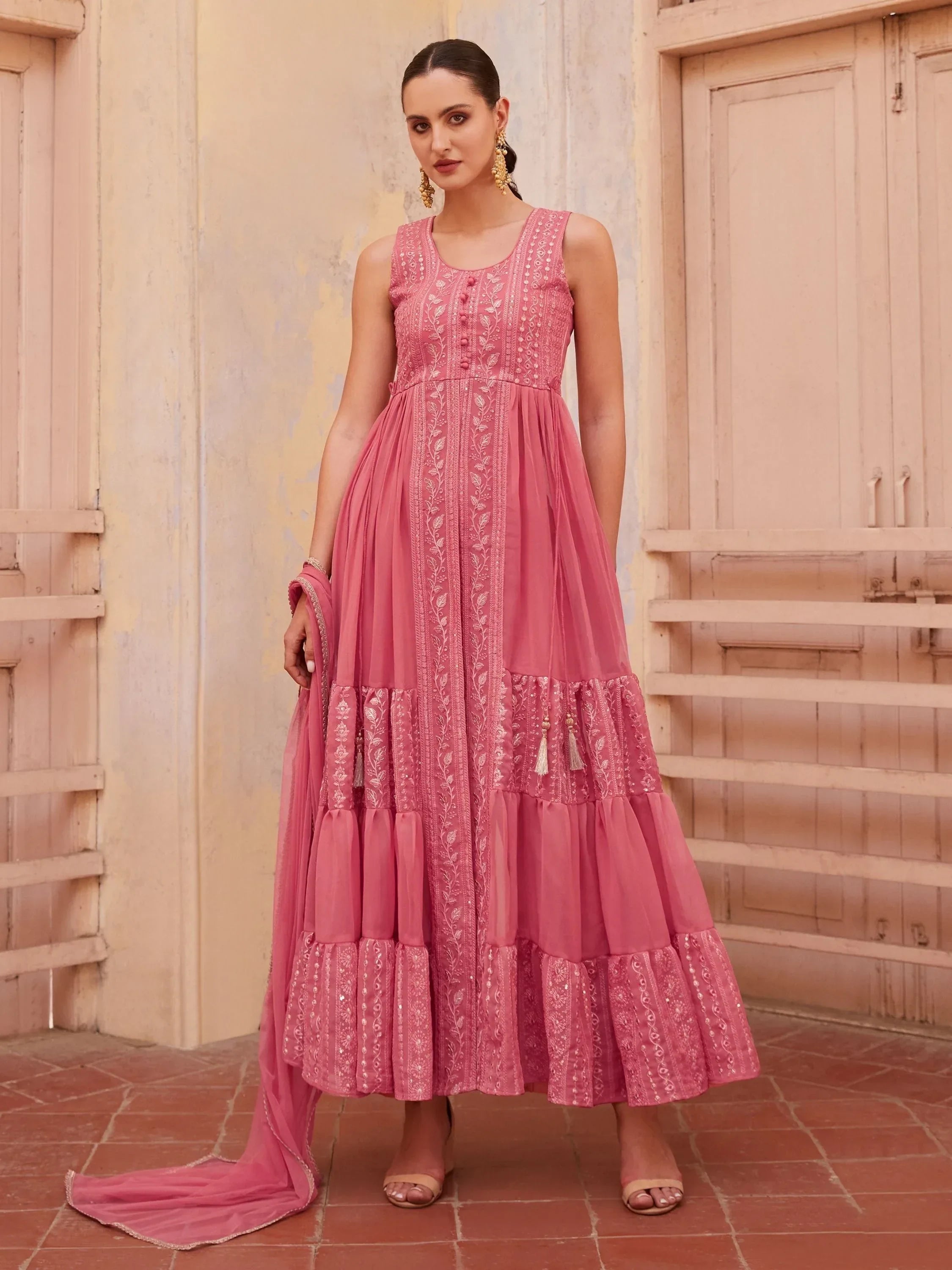 Woman wearing sleeveless pink embroidered ethnic gown with dupatta in traditional setting