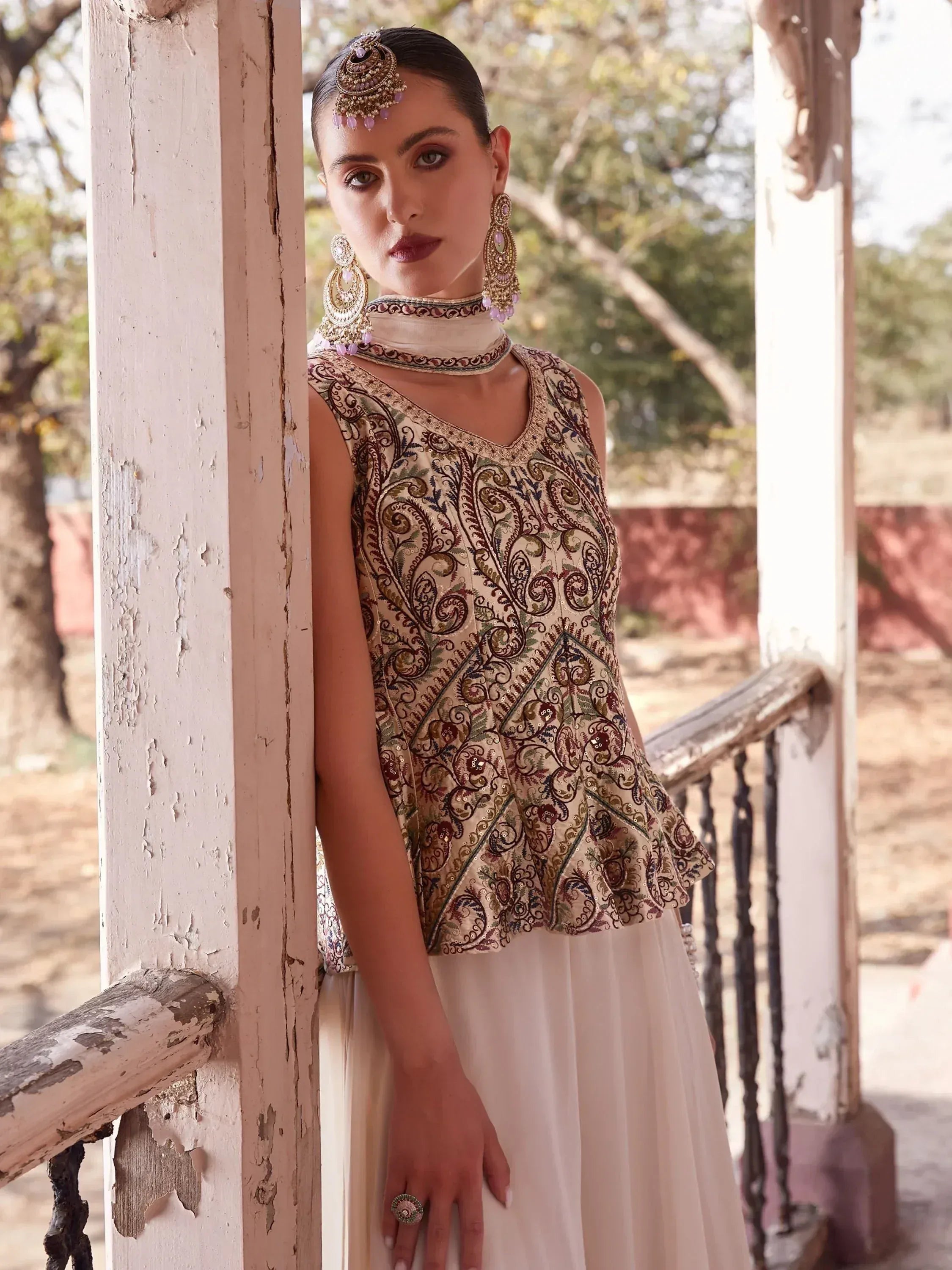 Woman wearing embroidered ethnic sleeveless blouse with cream skirt and traditional jewelry