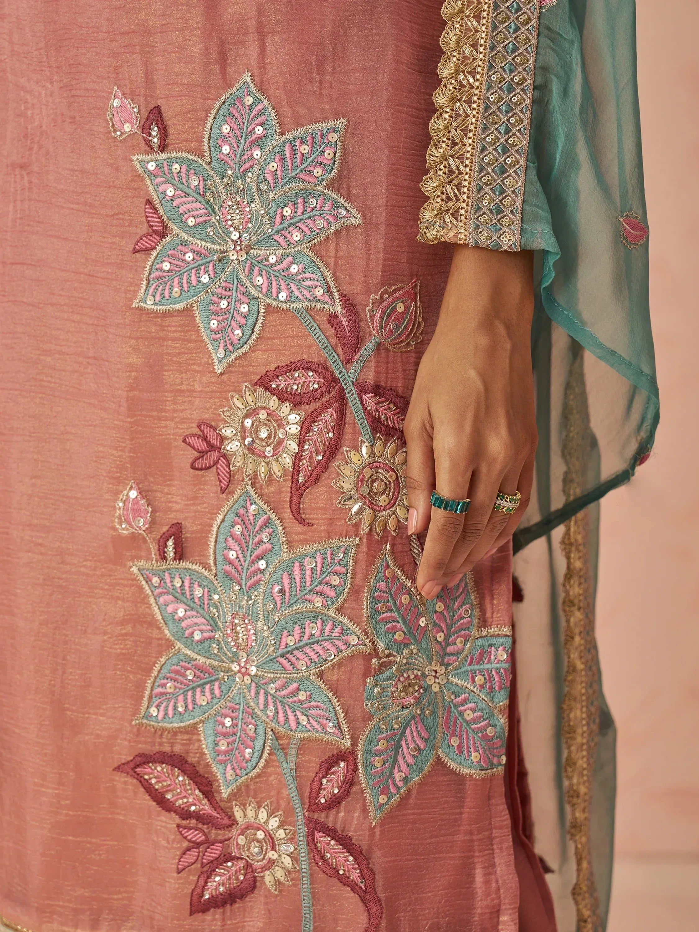 Pink ethnic gown with teal floral embroidery and gold detailing, paired with matching dupatta
