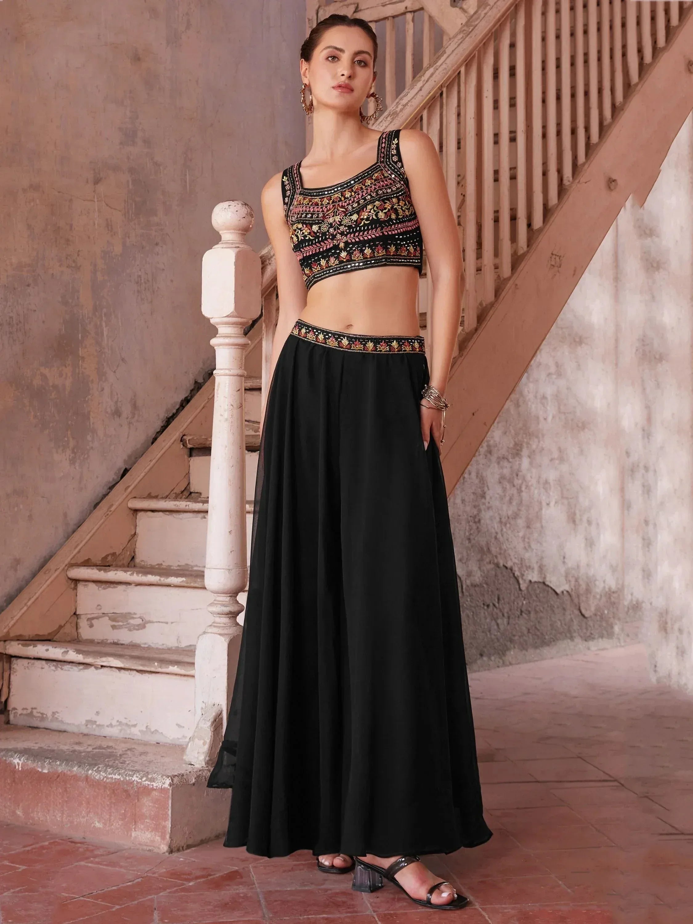 Woman wearing black embroidered lehenga choli set with ethnic jewelry, standing by stairs