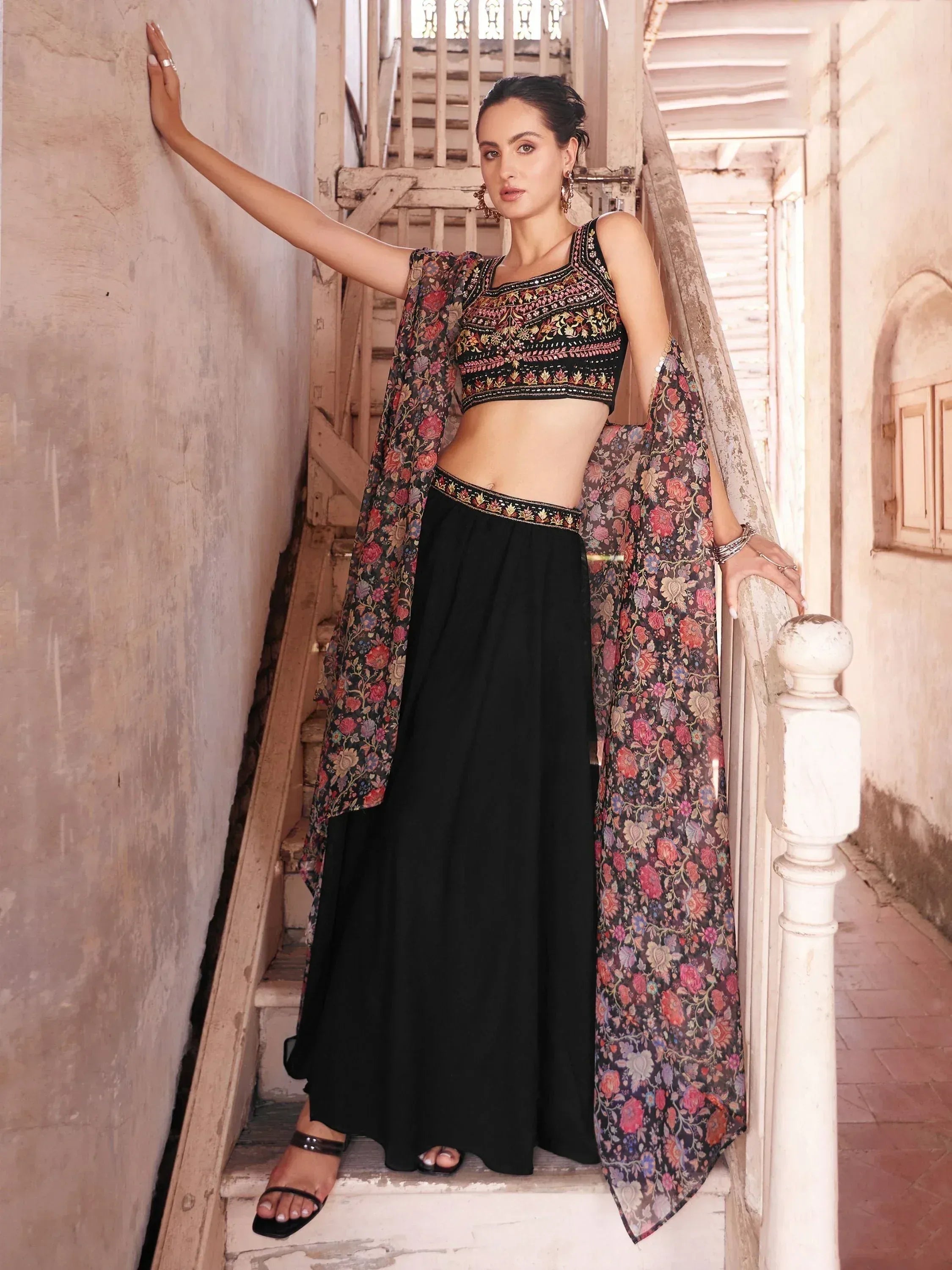 Woman wearing black embroidered lehenga choli with floral dupatta on stairs