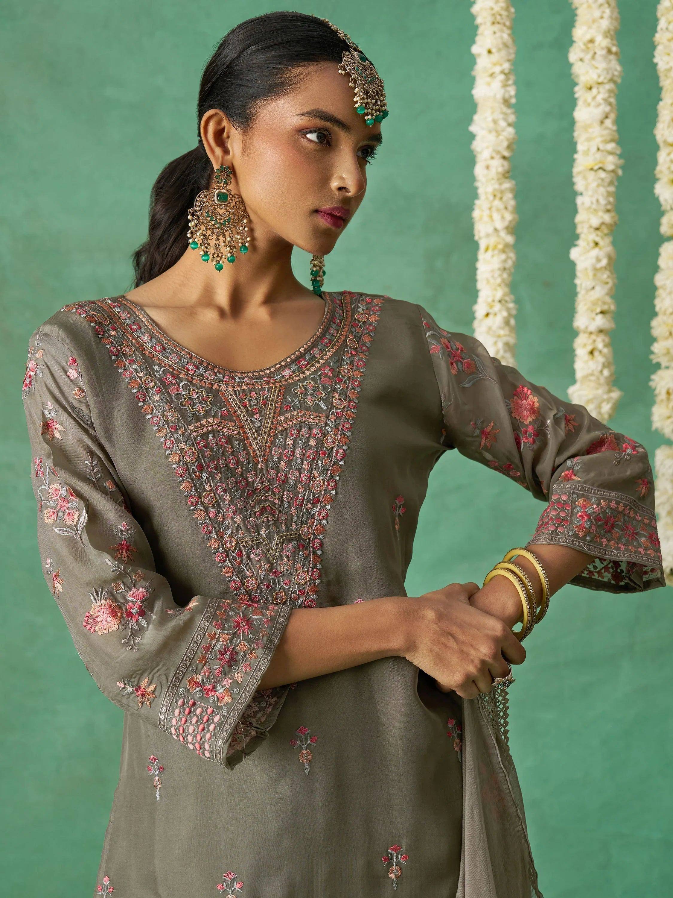 Woman in olive green embroidered ethnic kurta with floral details, traditional jewelry, and floral garlands.