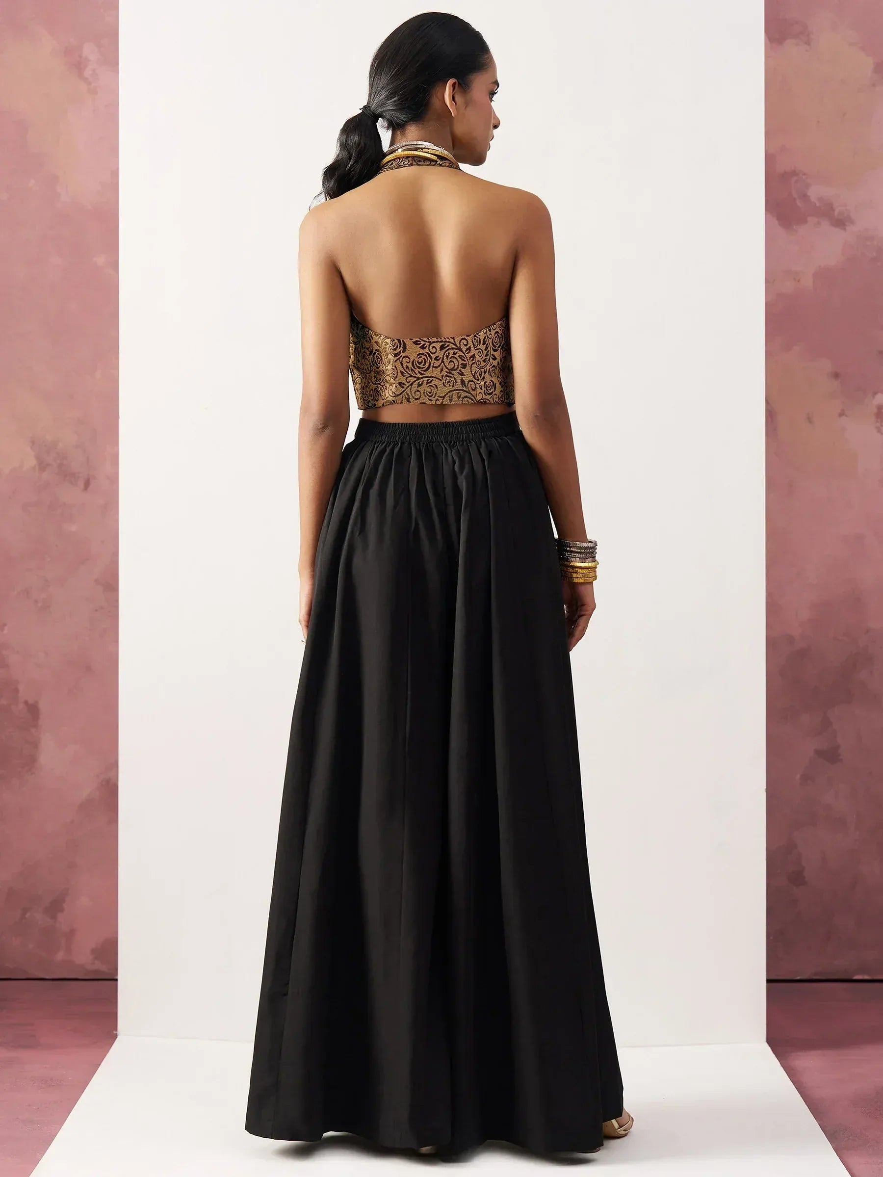 Back view of woman in black ethnic gown with gold embroidered crop top, perfect for Indian occasions.