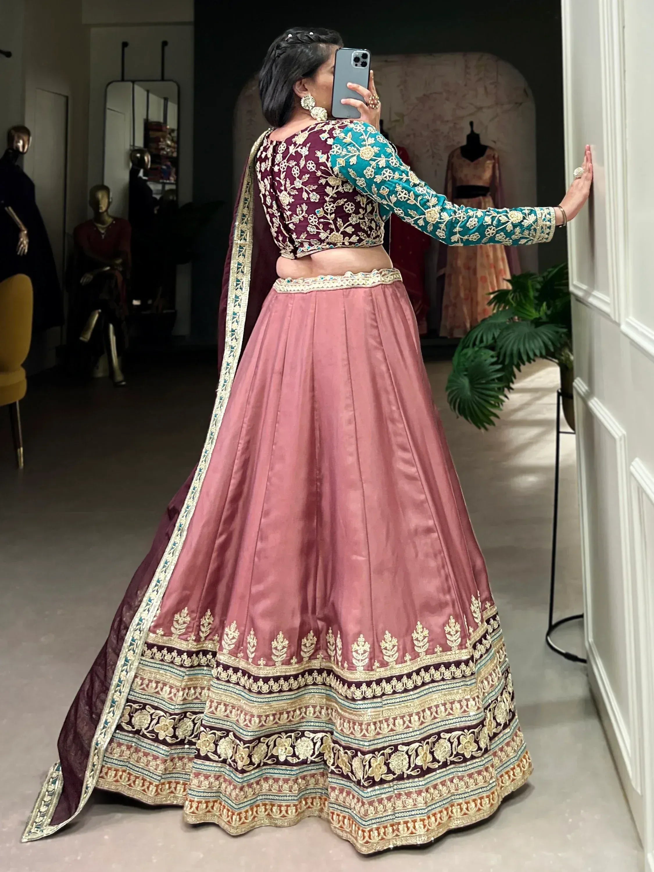 Woman taking mirror selfie in maroon and teal embroidered lehenga choli with pink skirt, ethnic Indian wear