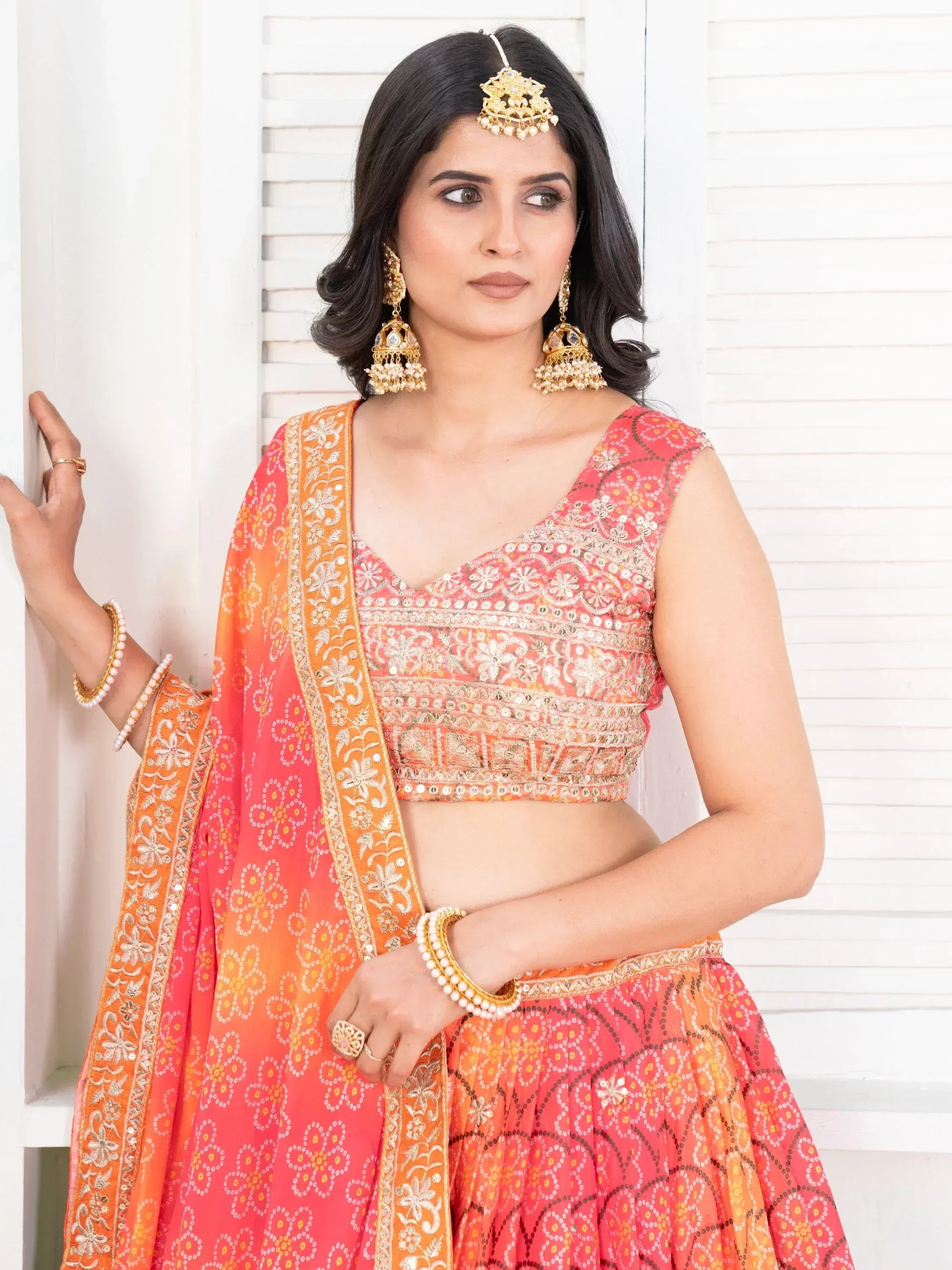 Woman in coral orange embroidered lehenga choli with gold jewelry, perfect for Indian ethnic occasions.