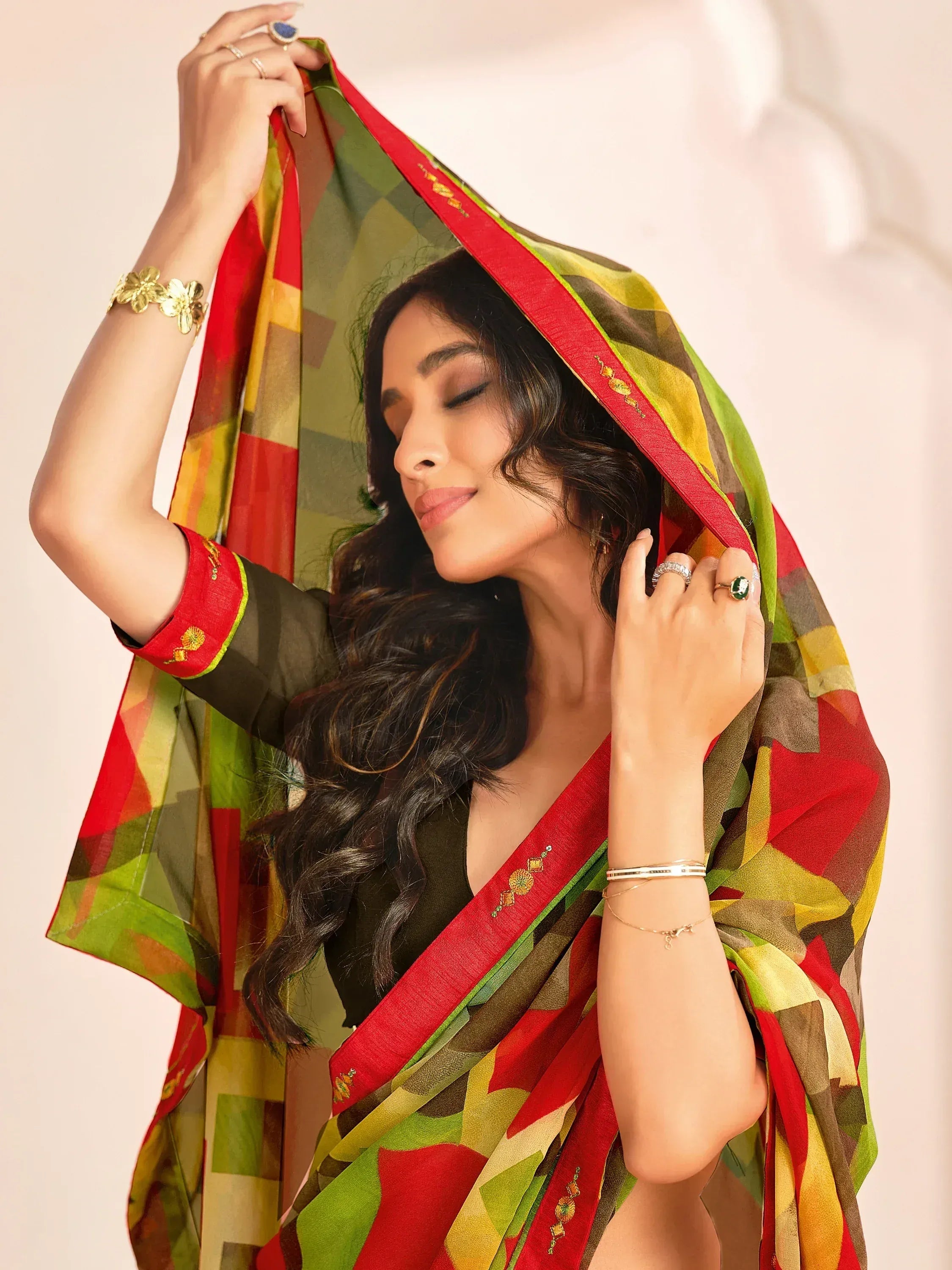 Woman in vibrant ethnic saree with geometric print, red border, and gold embroidery, styled with jewelry