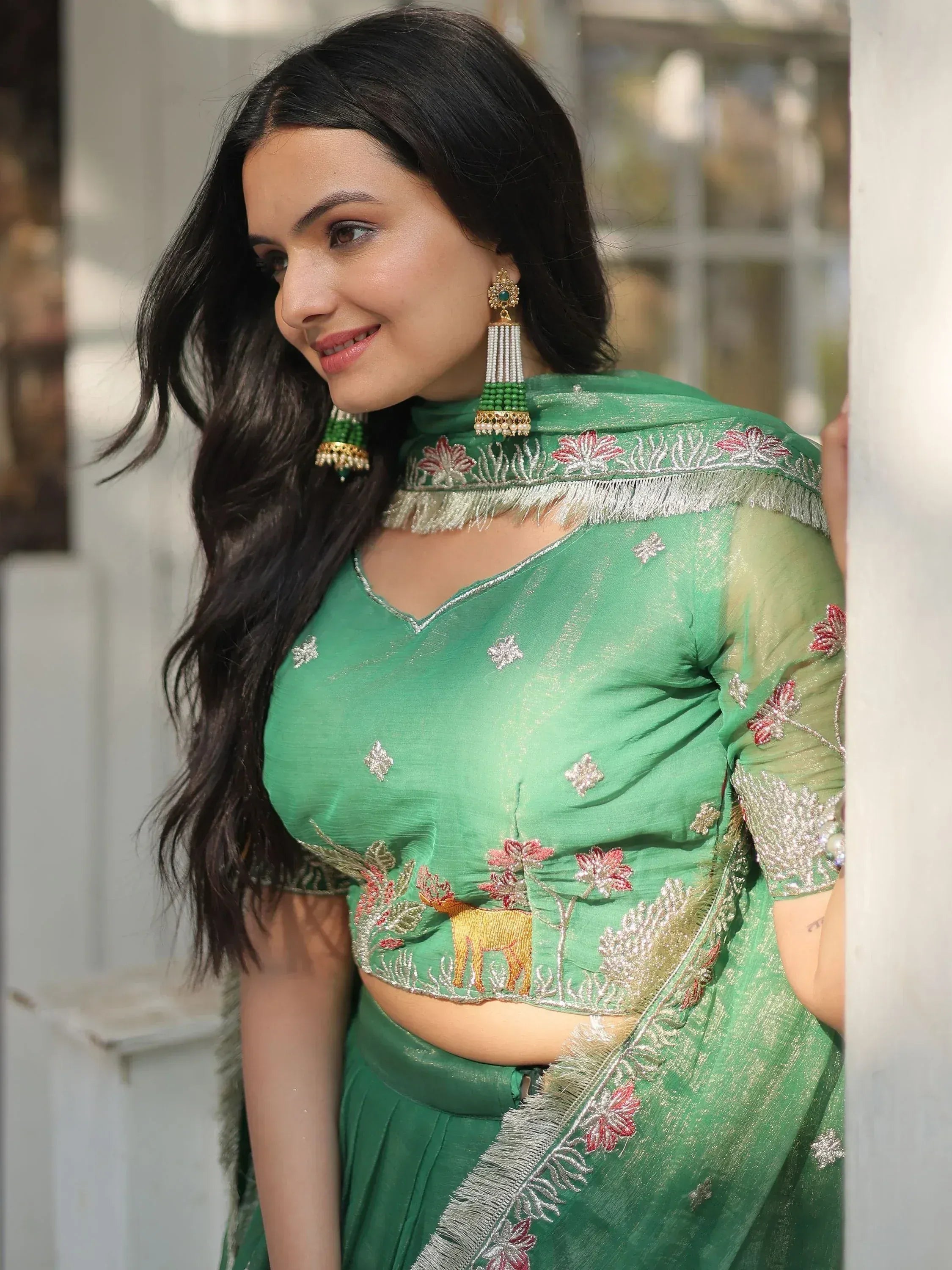 Green embroidered lehenga choli with deer motif, floral details, and matching earrings for Indian ethnic wear.