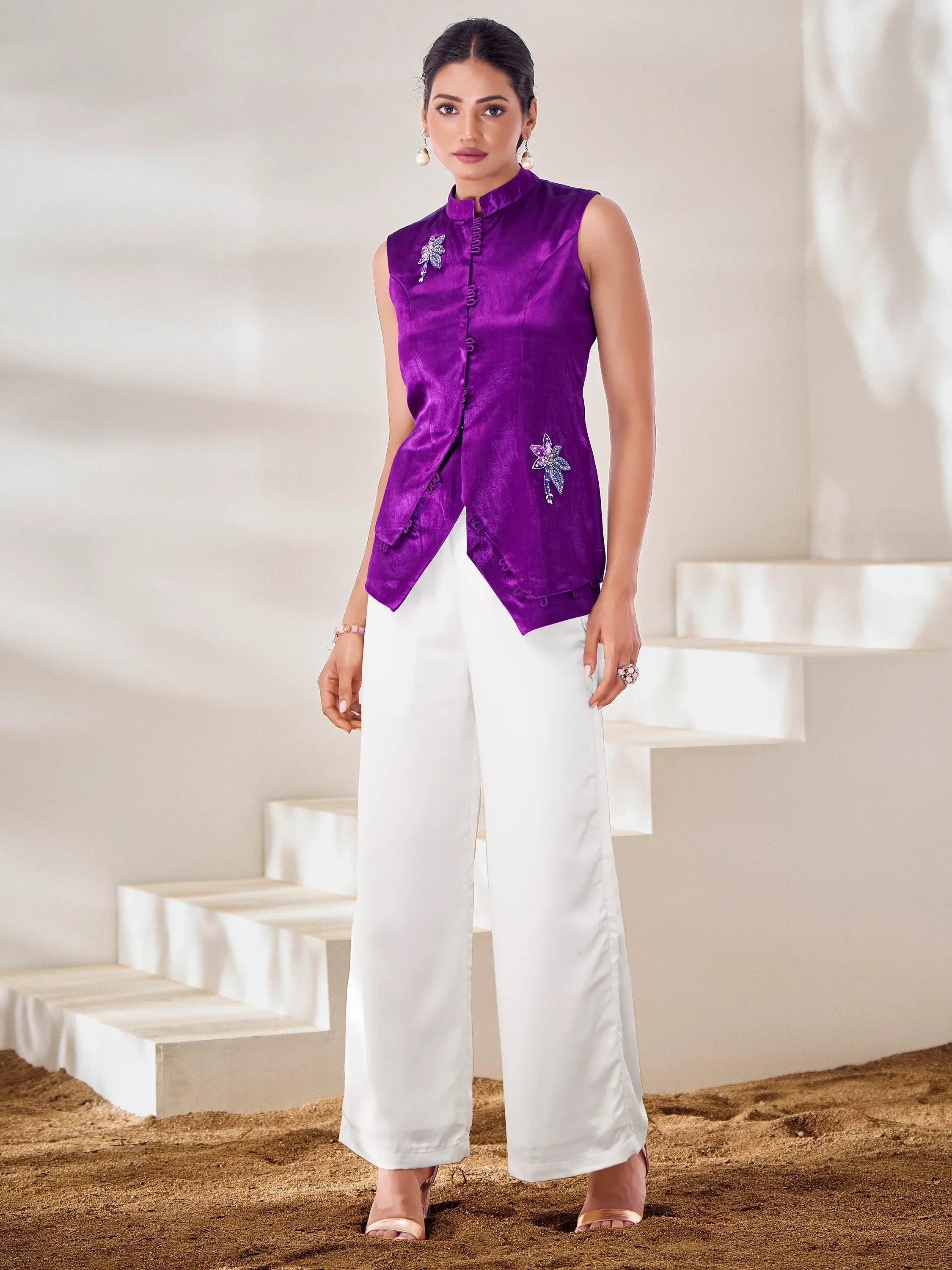 Woman in a sleeveless purple embroidered ethnic top and white palazzo pants, standing indoors
