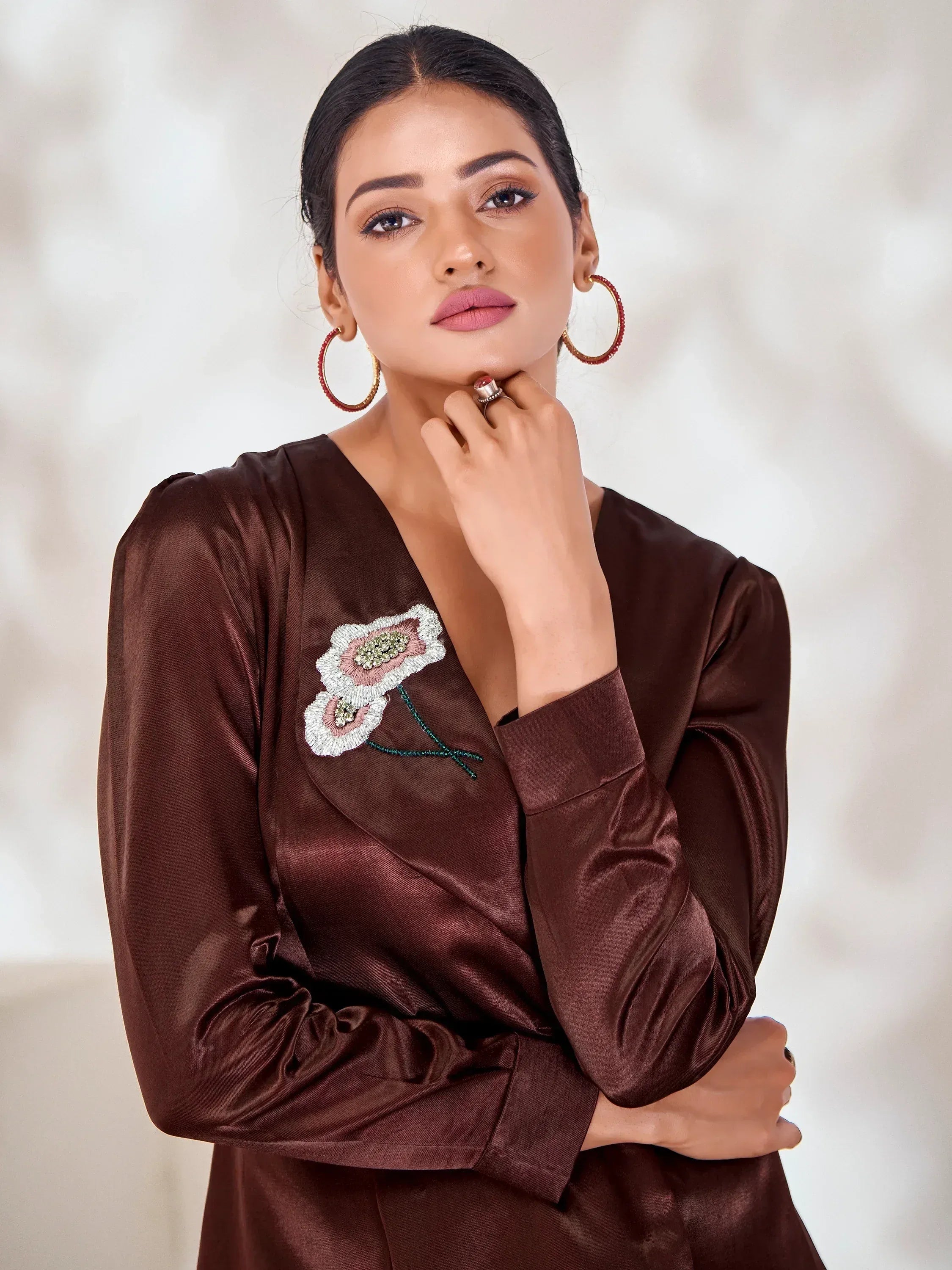 Woman in brown satin ethnic top with floral embroidery, styled with hoop earrings for festive occasions.