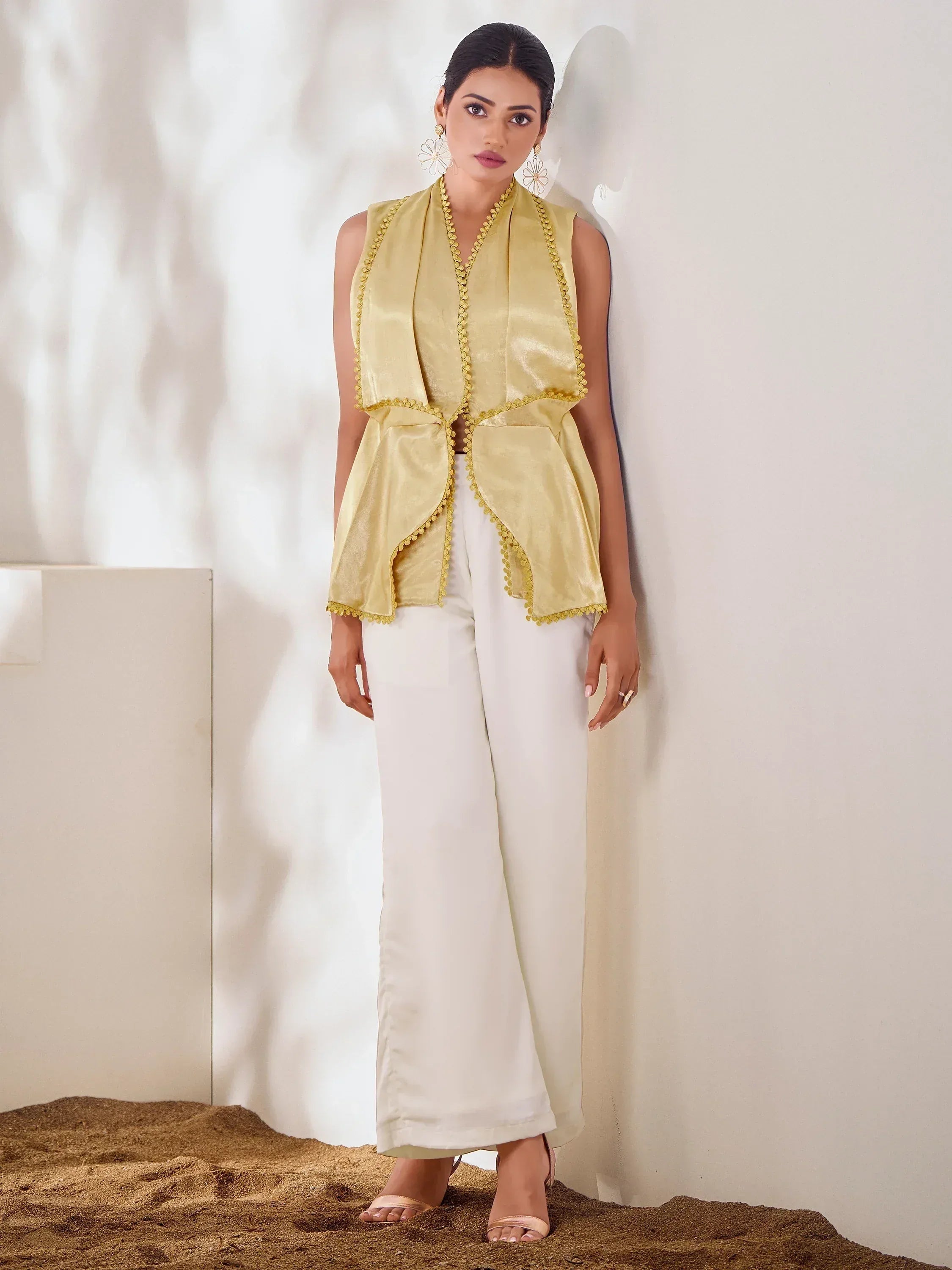 Yellow sleeveless ethnic vest with pom-pom trim paired with white palazzo pants, styled for modern Indian wear.