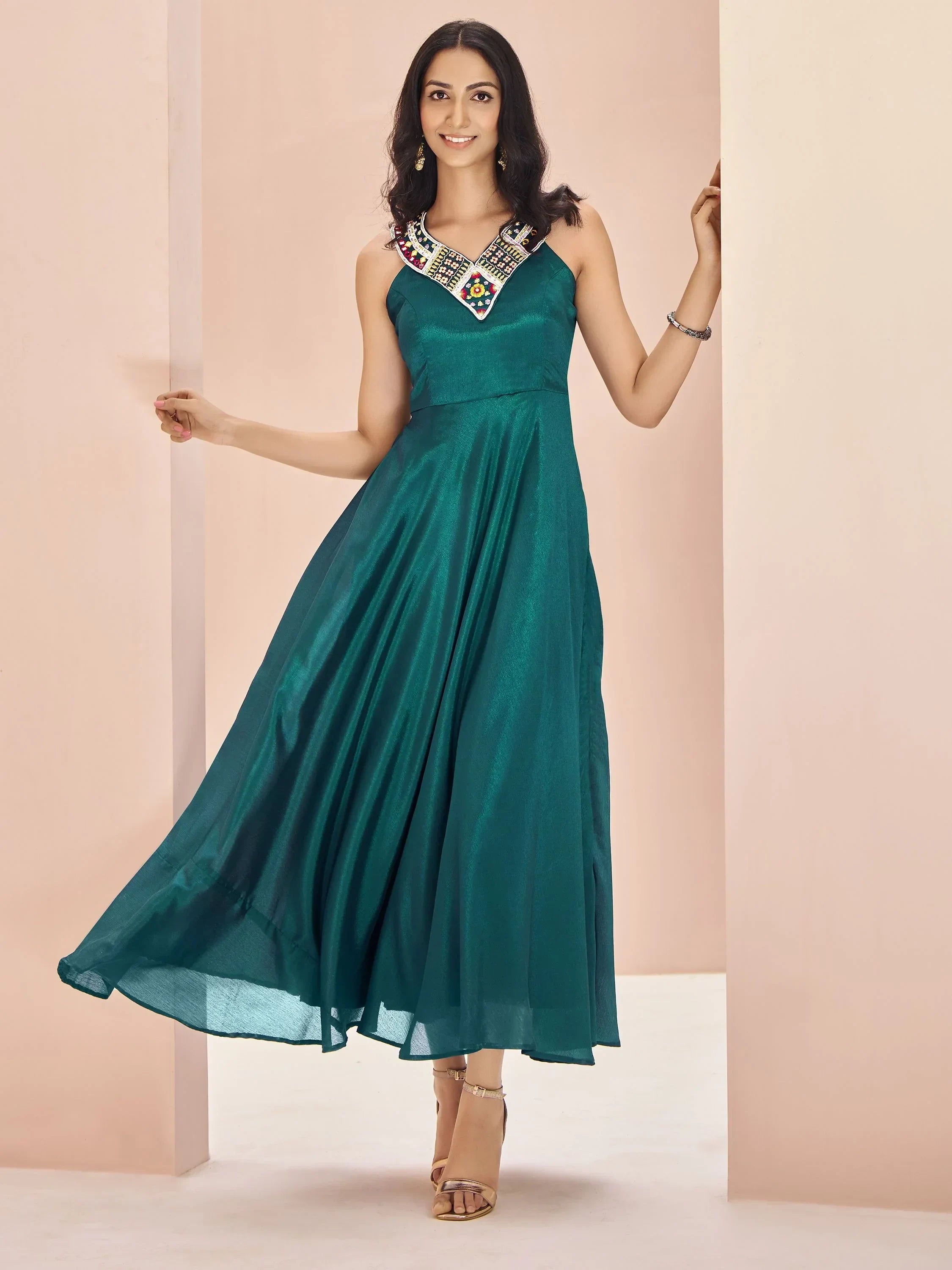 Woman in teal ethnic gown with embroidered neckline, sleeveless, standing indoors