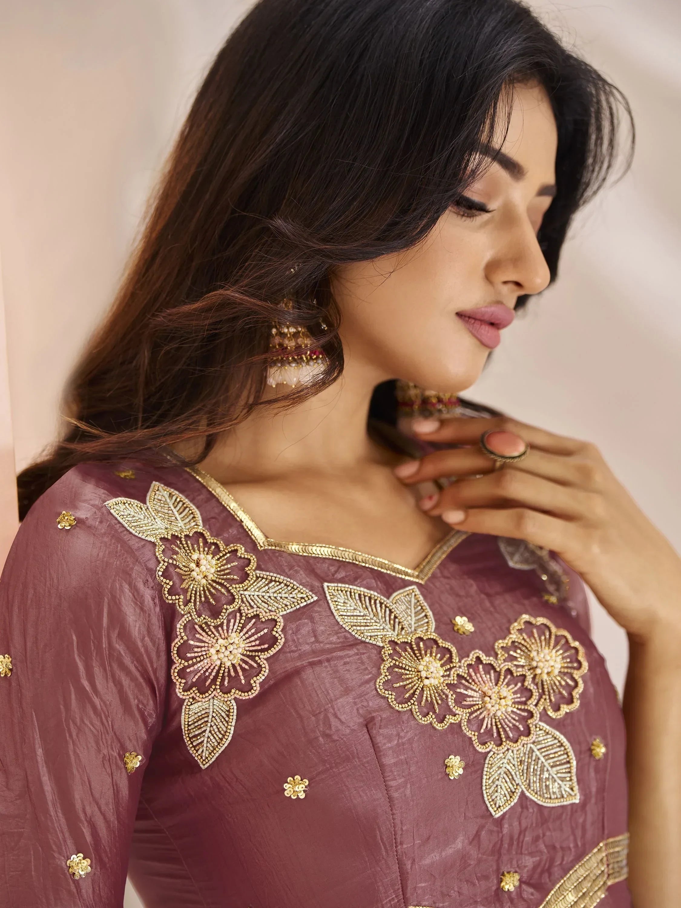 Woman wearing mauve embroidered ethnic gown with gold floral details and statement earrings