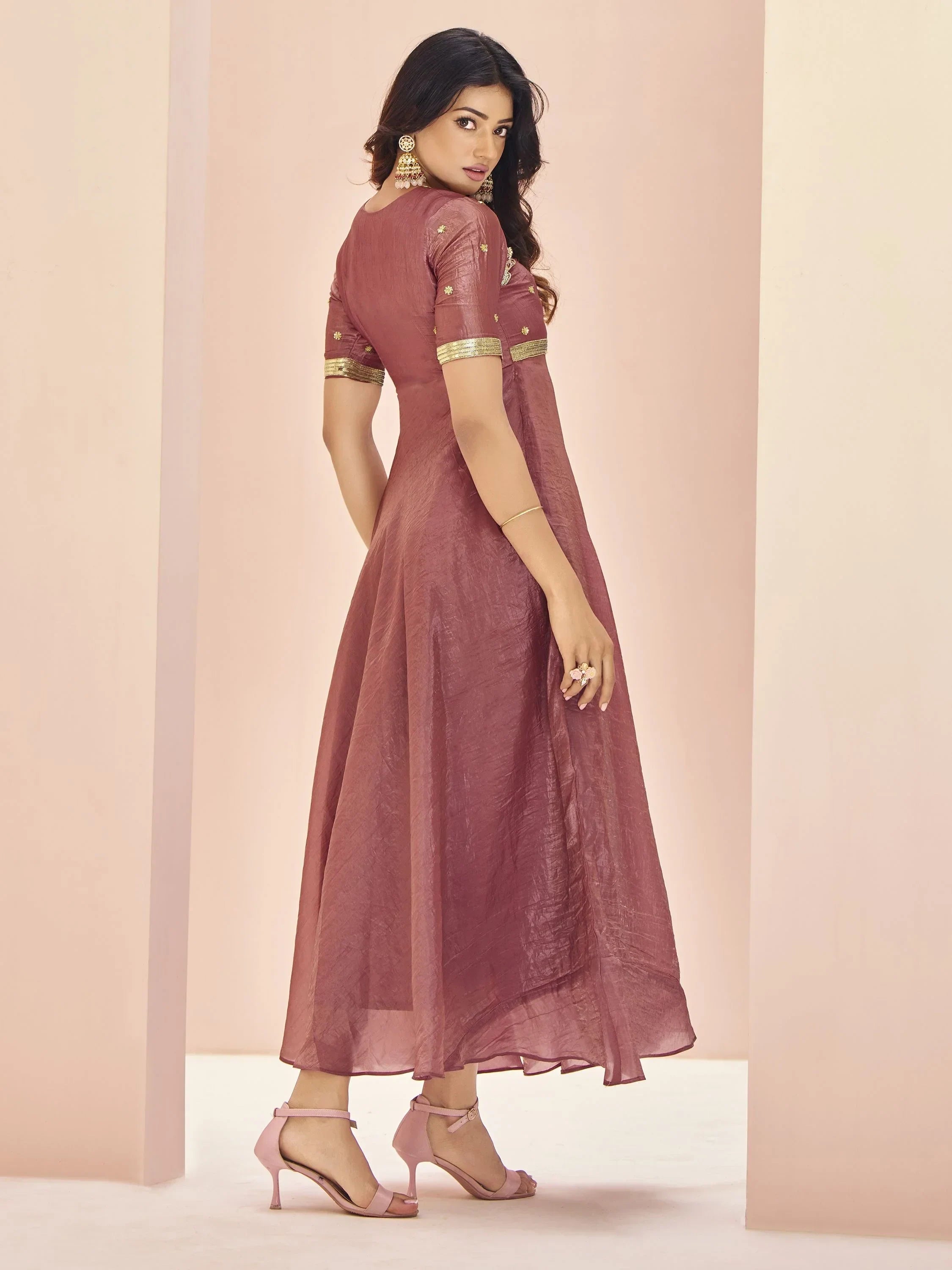 Woman in mauve ethnic gown with gold detailing and pink heels, posing indoors