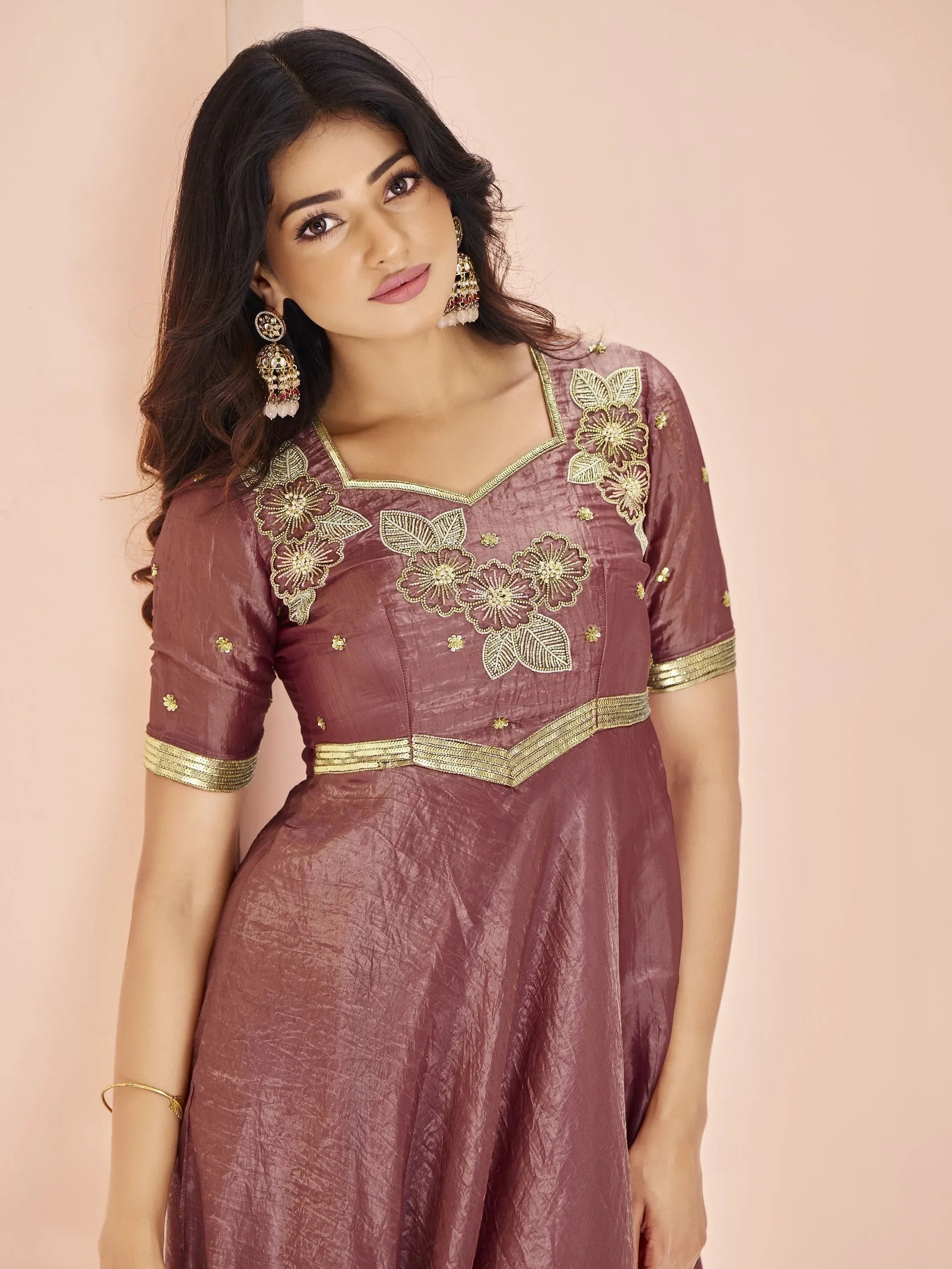 Woman in maroon embroidered ethnic gown with gold floral patterns, traditional jewelry