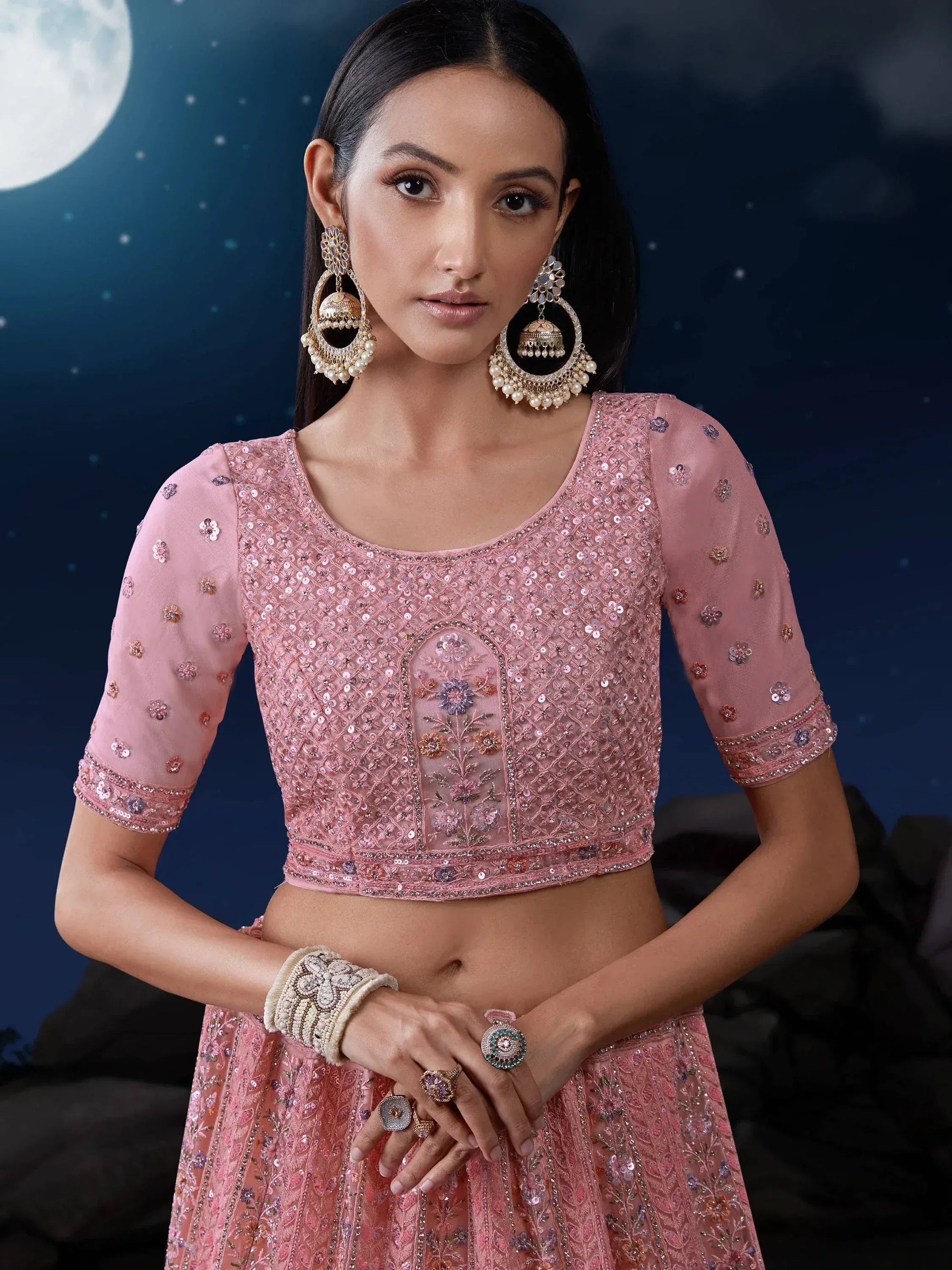 Pink embroidered lehenga choli with sequins, floral motifs, and jhumka earrings under moonlit sky