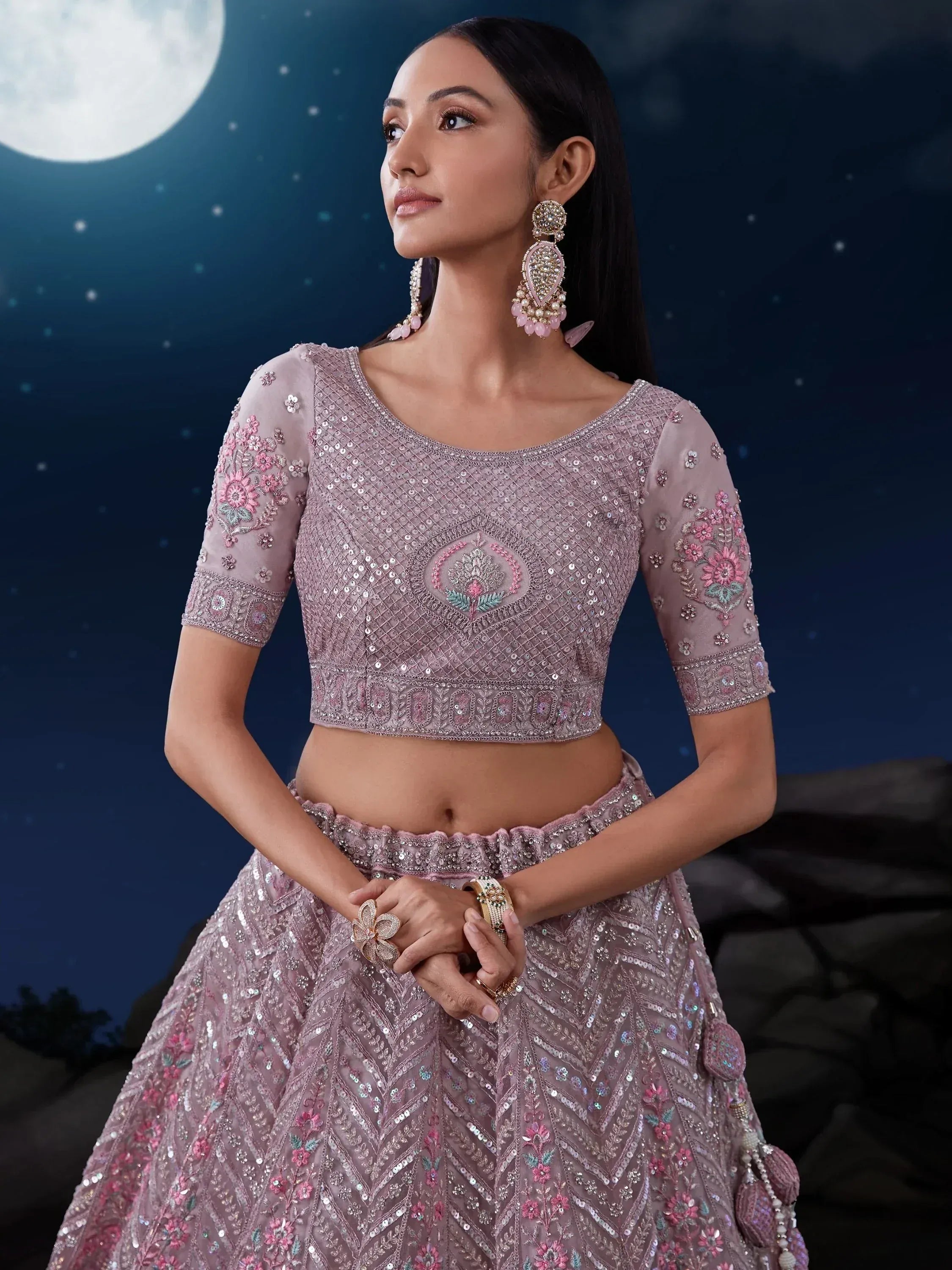 Elegant pink embroidered lehenga choli with sequins, floral motifs, and statement earrings under moonlight