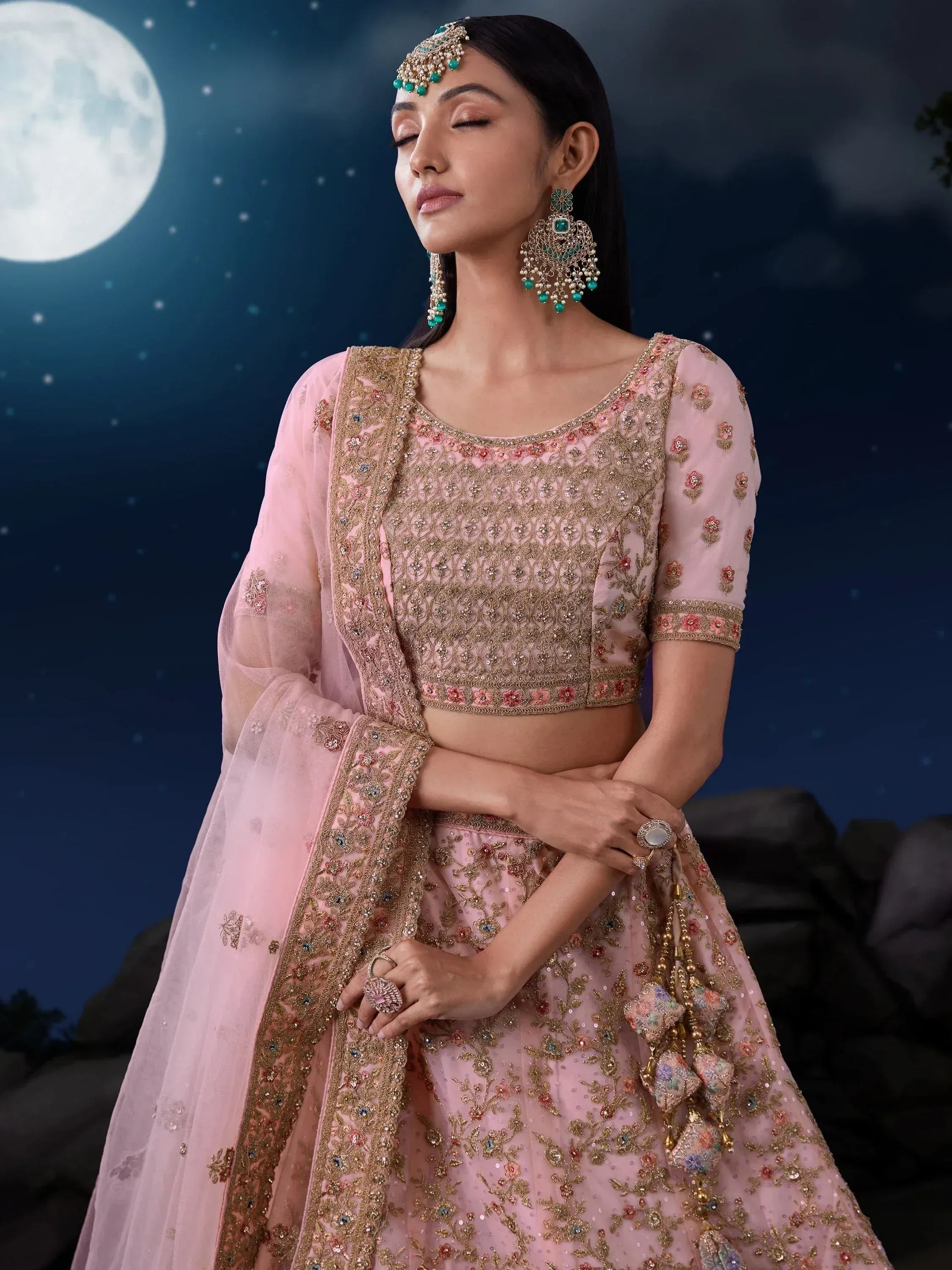 Pink embroidered lehenga choli with gold detailing, perfect for Indian weddings or festive occasions under moonlight.