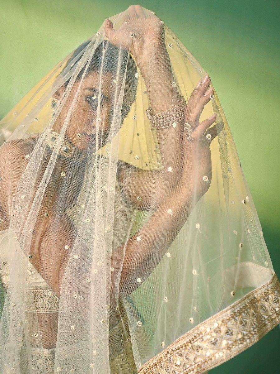 Elegant Indian bride in cream lehenga with gold embroidery, sheer dupatta, and traditional jewelry