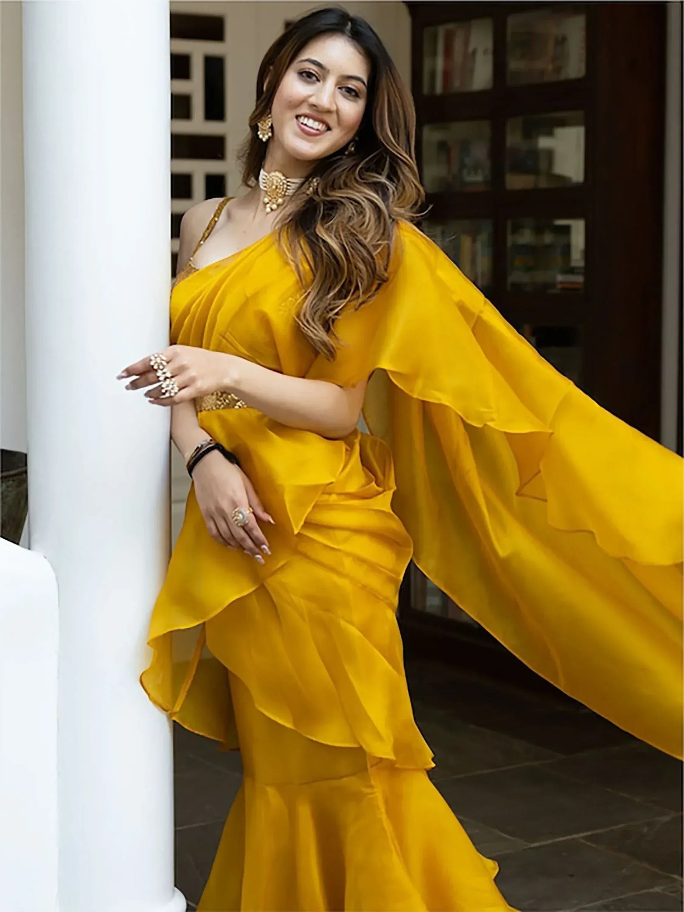 Woman in vibrant yellow ethnic gown with ruffled sleeves and gold jewelry, perfect for festive occasions.
