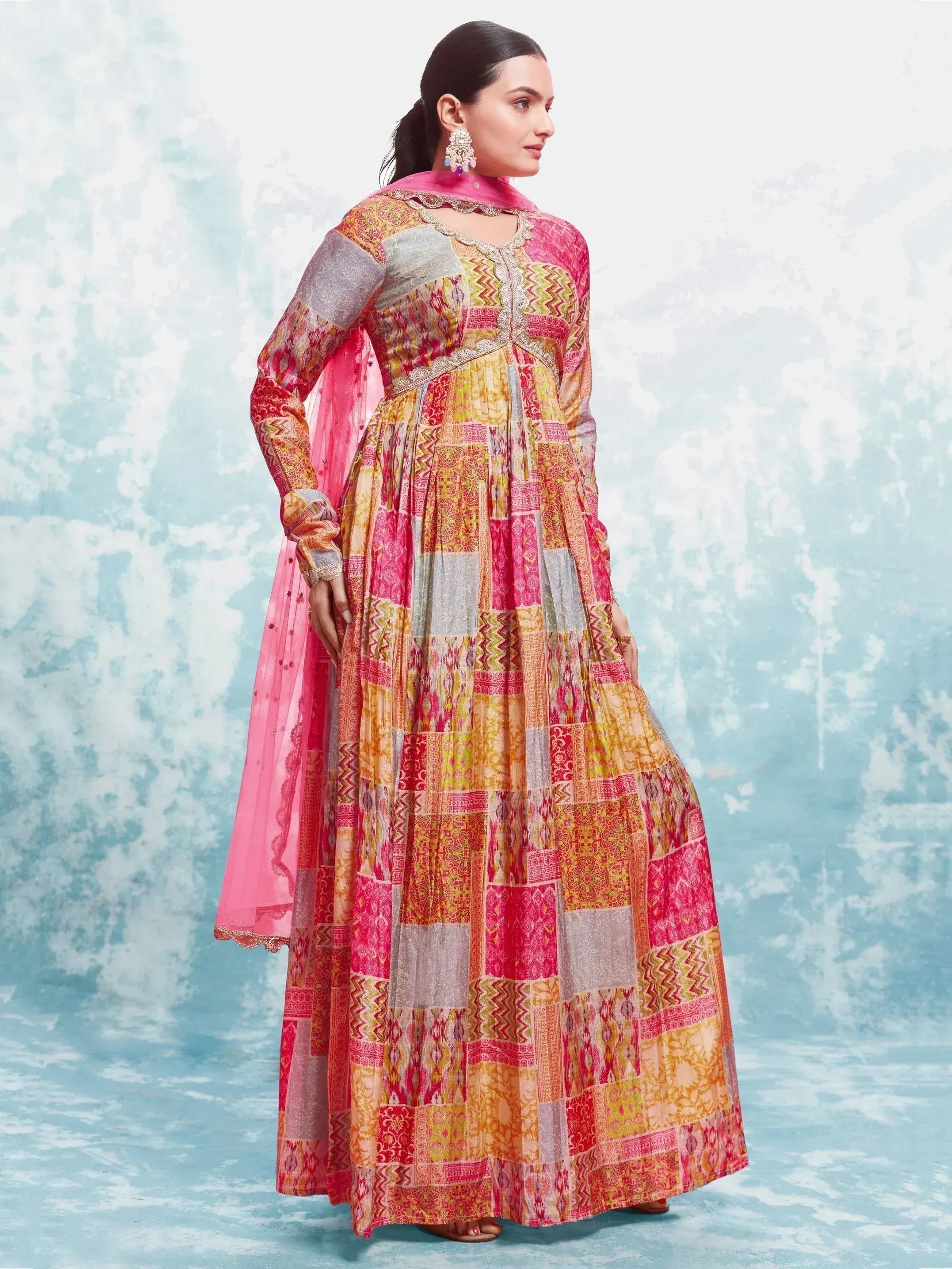 Woman wearing colorful patchwork printed Anarkali suit with pink dupatta and earrings