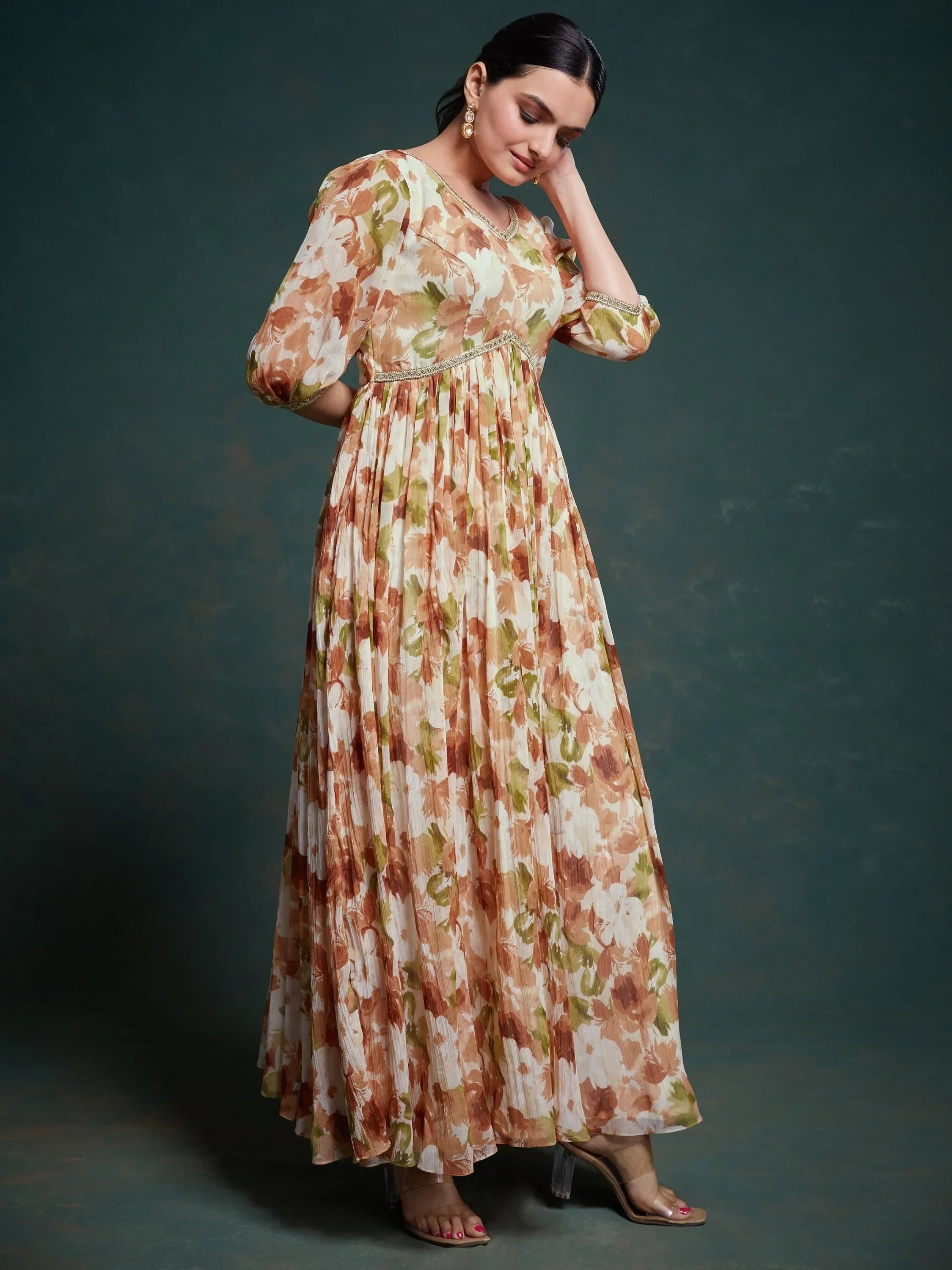 Woman wearing a floral printed ethnic gown with sheer sleeves, standing indoors.