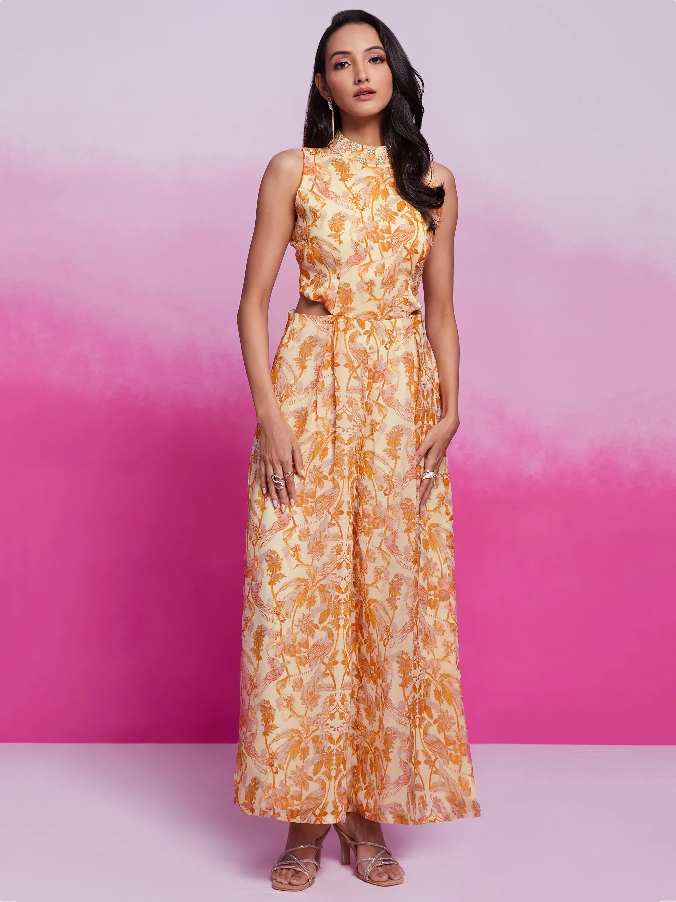 Woman wearing sleeveless yellow floral ethnic gown with cutout waist, pink background
