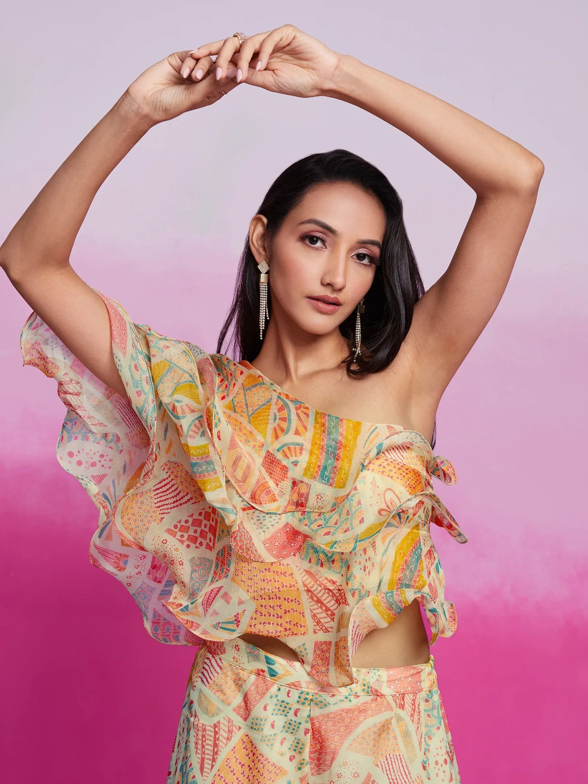 Woman in colorful printed one-shoulder ethnic dress against pink background