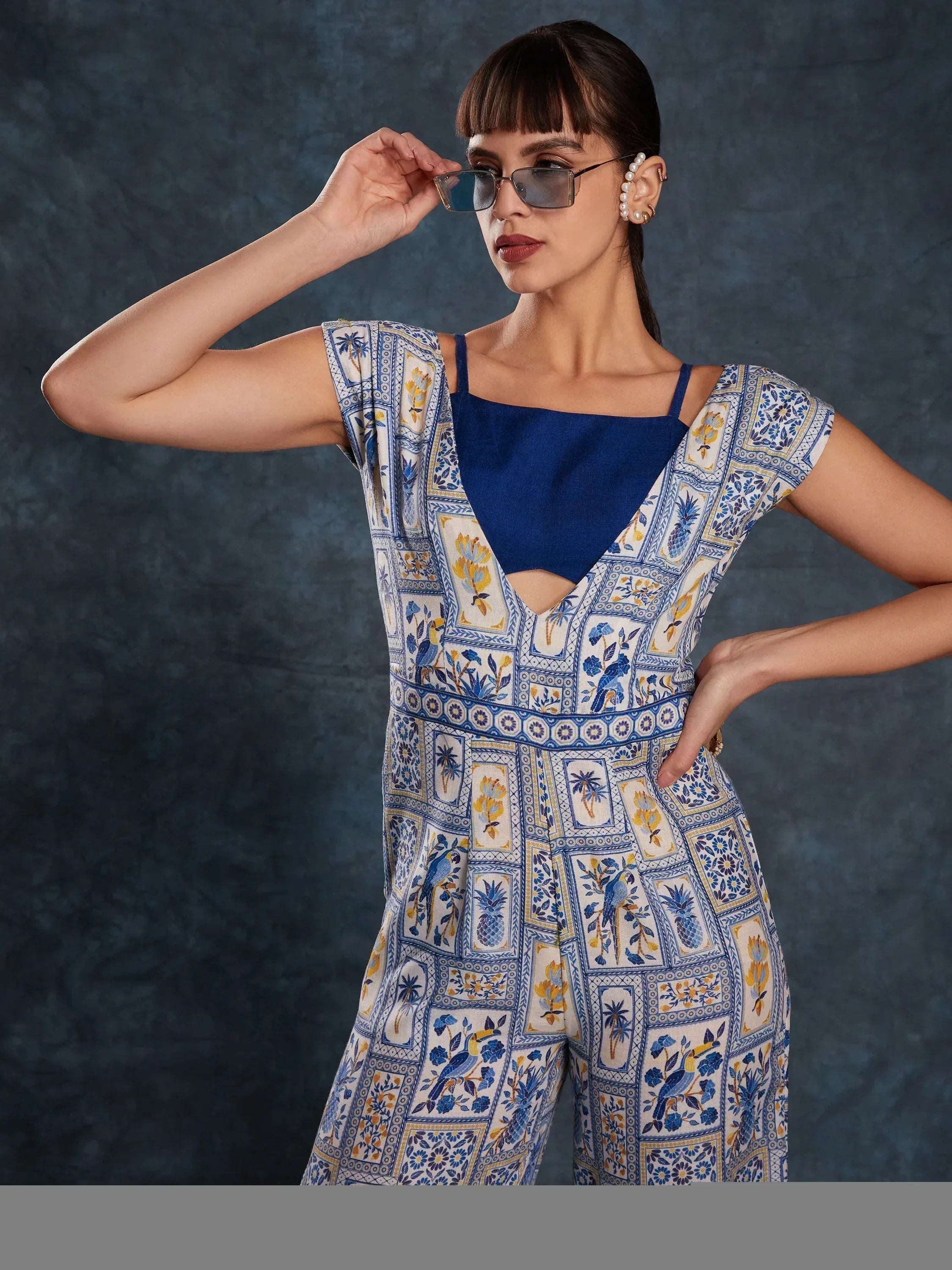 Blue and white printed ethnic jumpsuit with floral and bird motifs, paired with sunglasses and pearl earrings