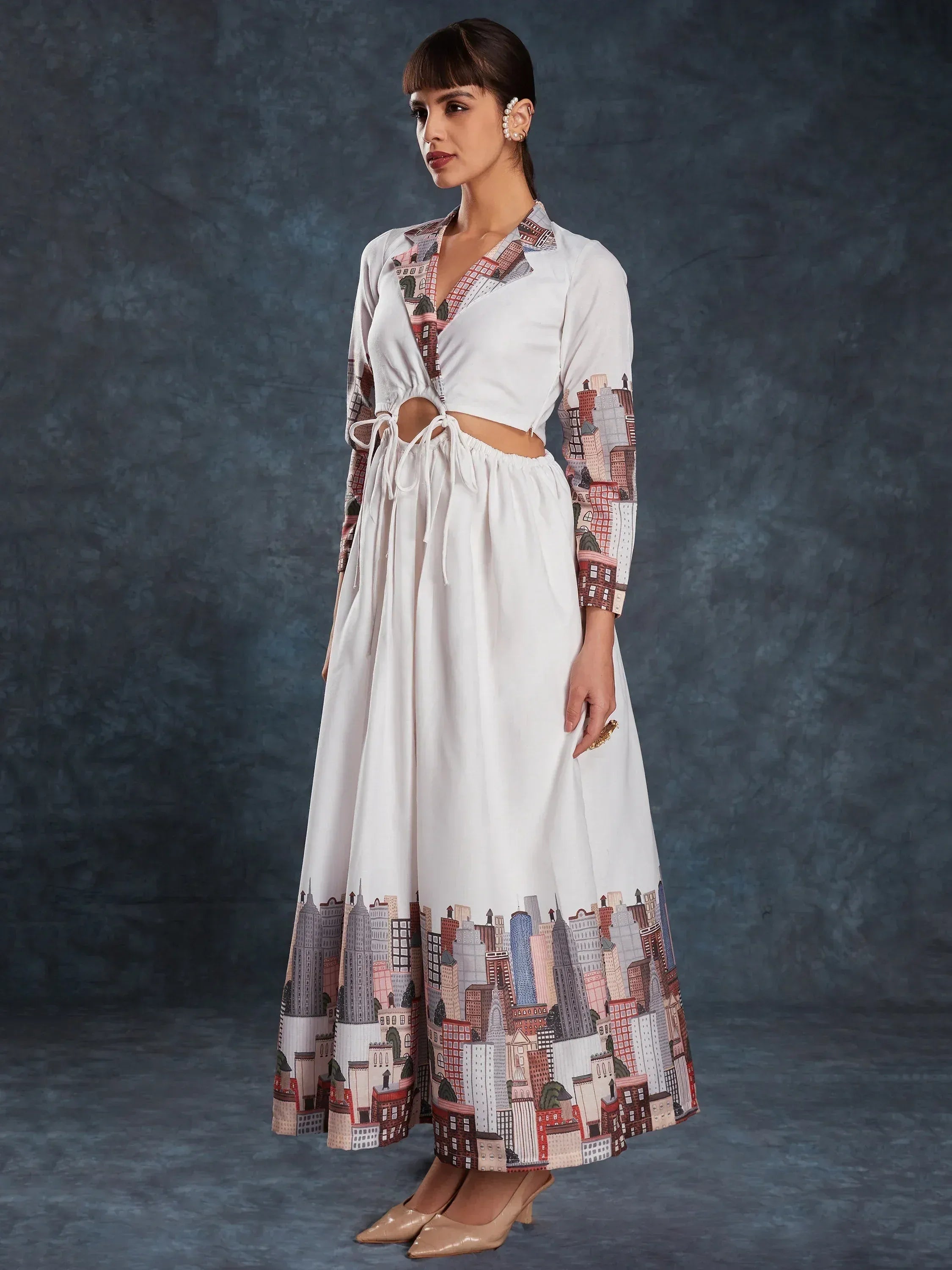 White ethnic gown with cityscape print, side cutouts, and tie waist, paired with pearl earrings