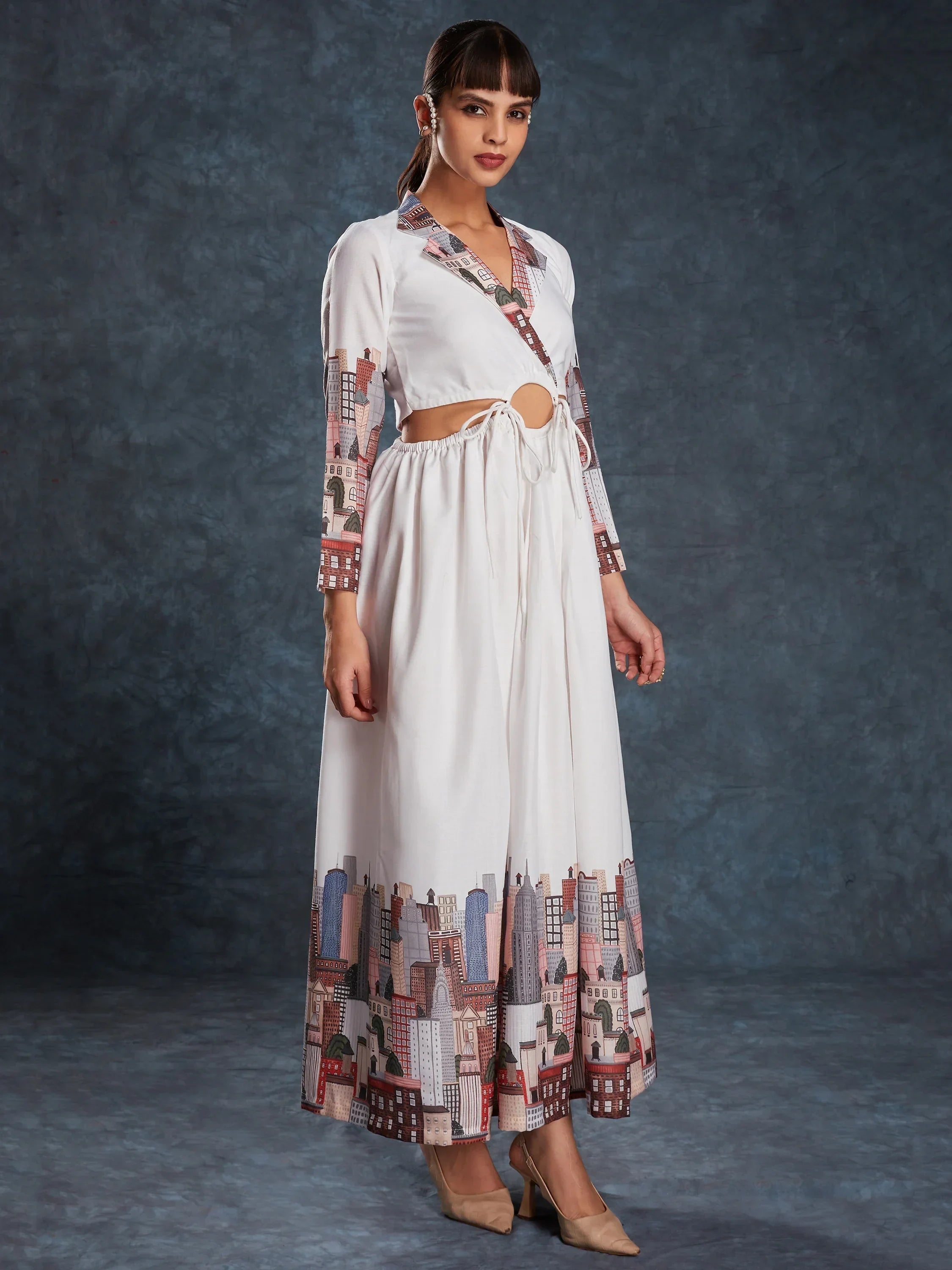 Woman in white long ethnic gown with cityscape print and tie detail, standing on studio backdrop