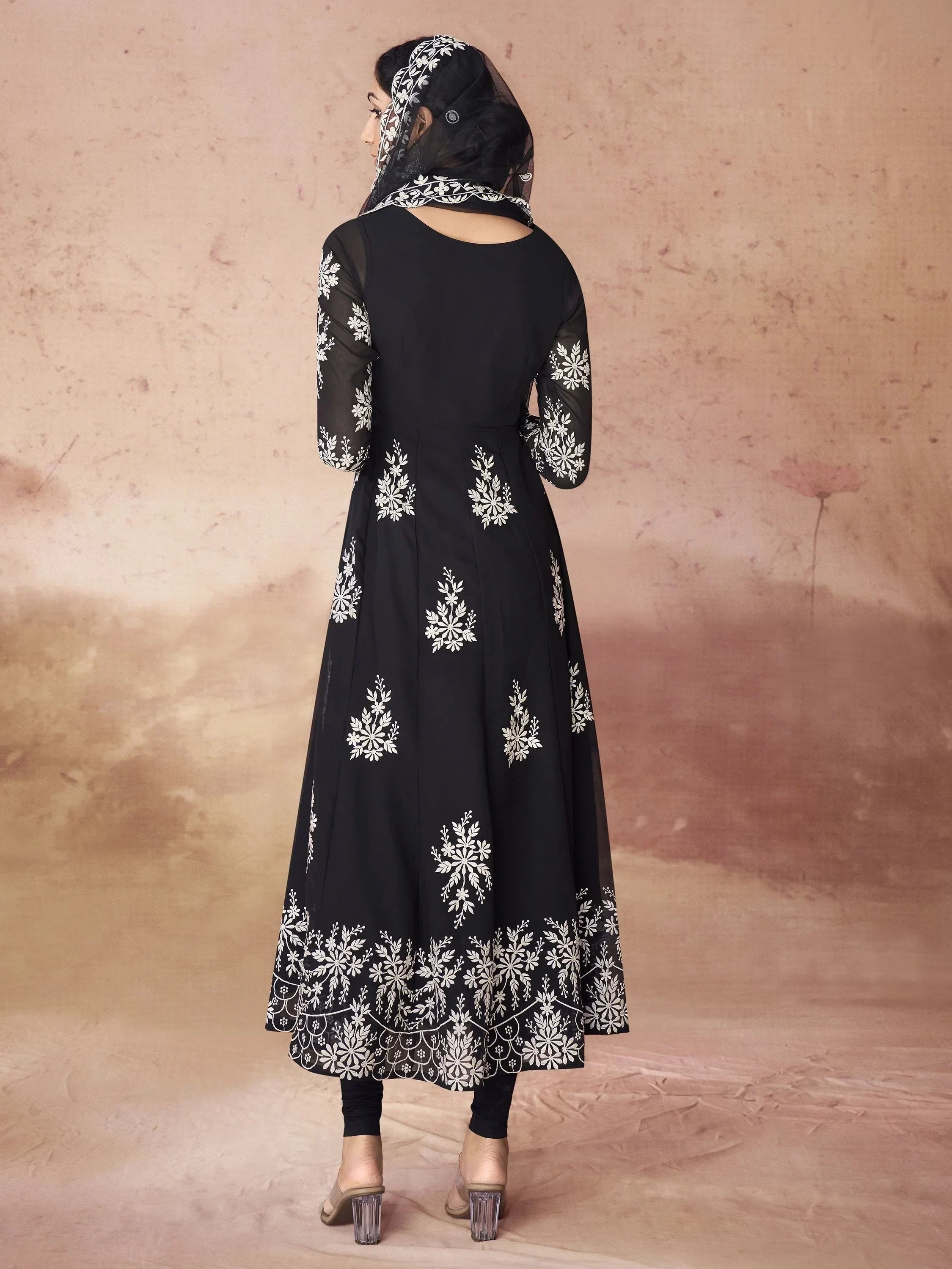 Woman in black embroidered Anarkali suit with dupatta, standing in front of a beige backdrop