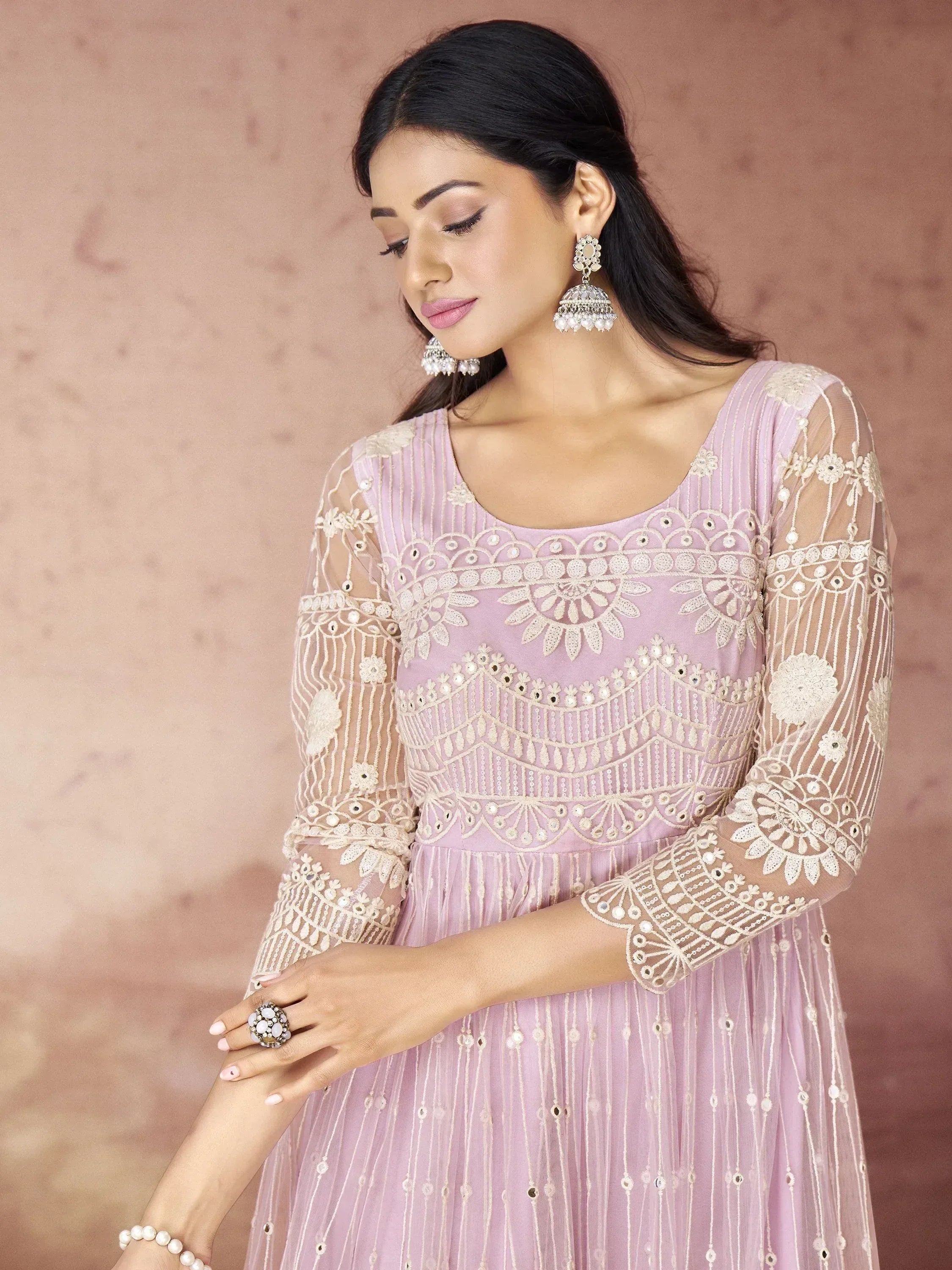 Elegant lavender ethnic gown with intricate white embroidery and sheer sleeves, paired with traditional jhumka earrings.