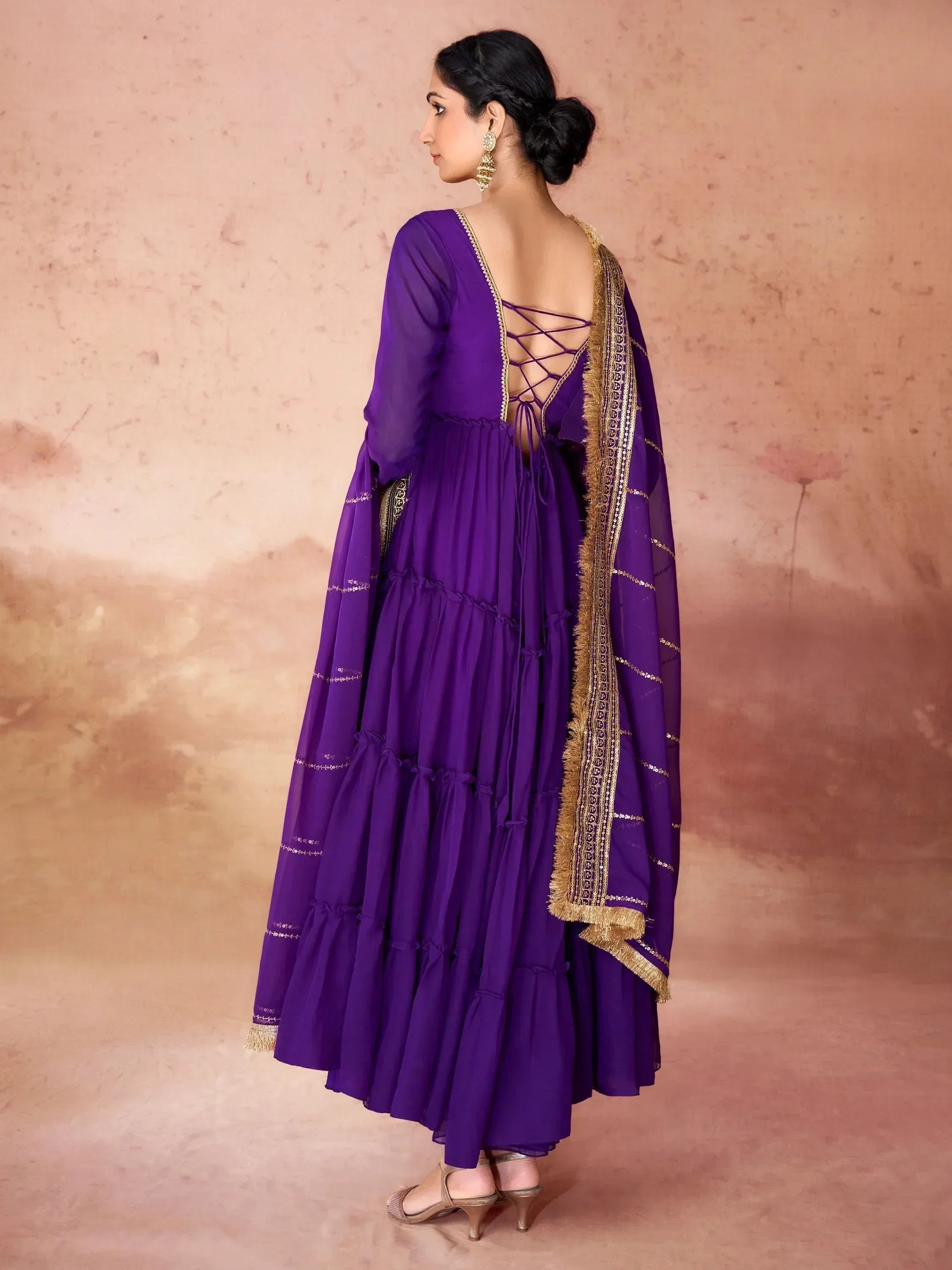 Woman in purple ethnic gown with gold dupatta and back lace-up detail, side profile