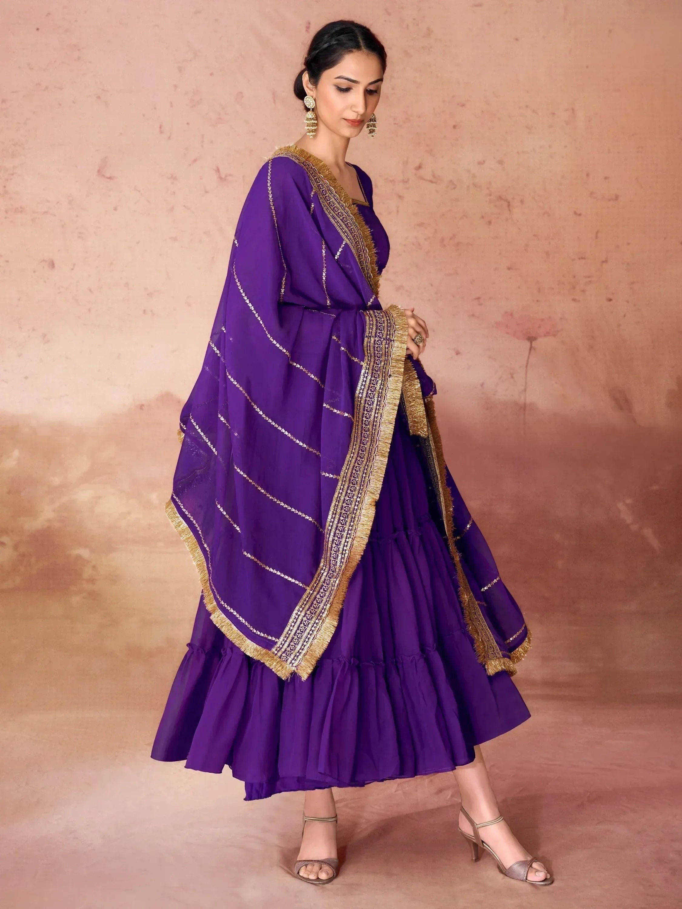 Woman wearing a purple Indian ethnic gown with gold border dupatta and statement earrings