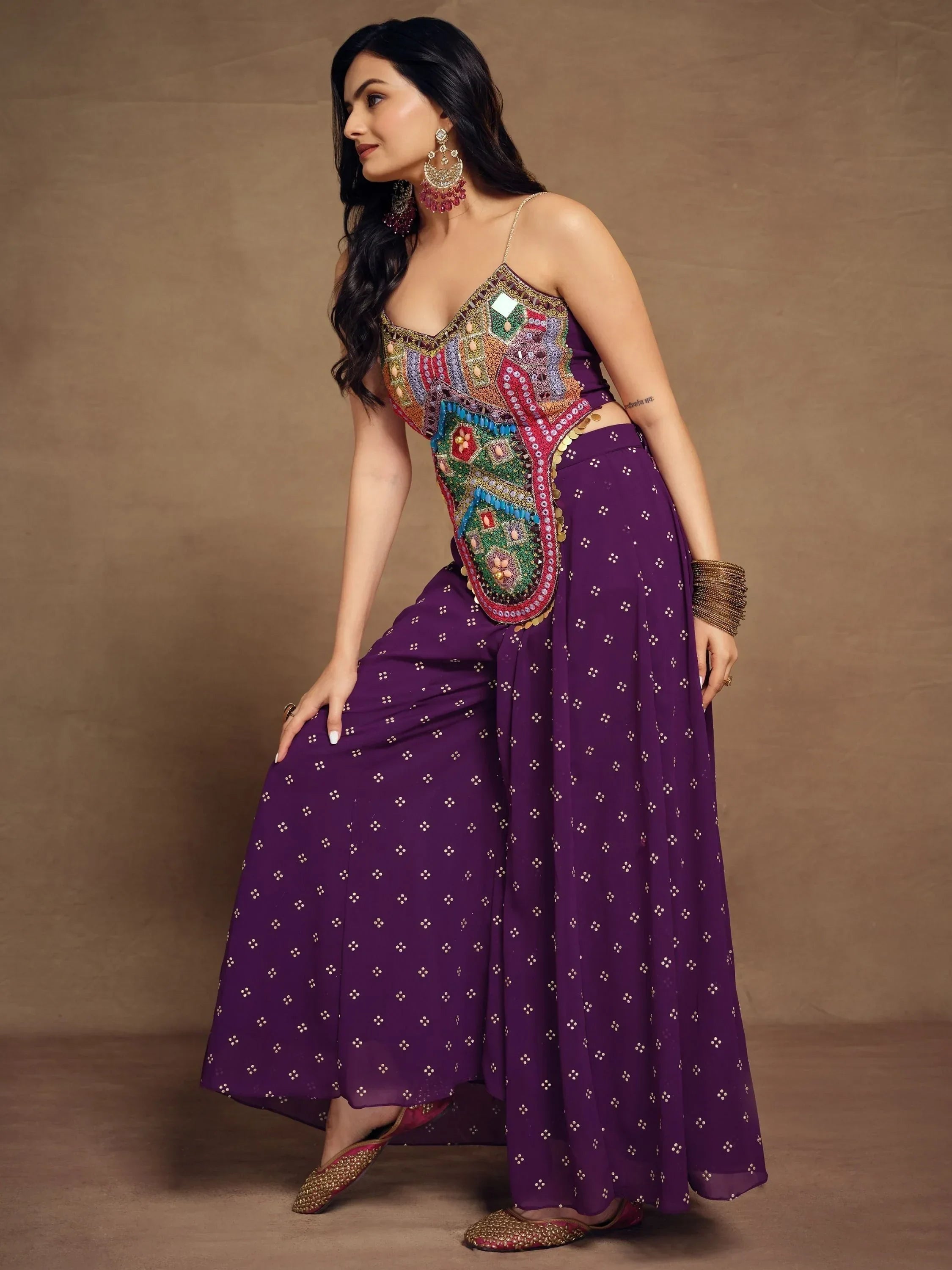 Woman in purple ethnic sharara set with colorful embroidered mirror work top, posing indoors
