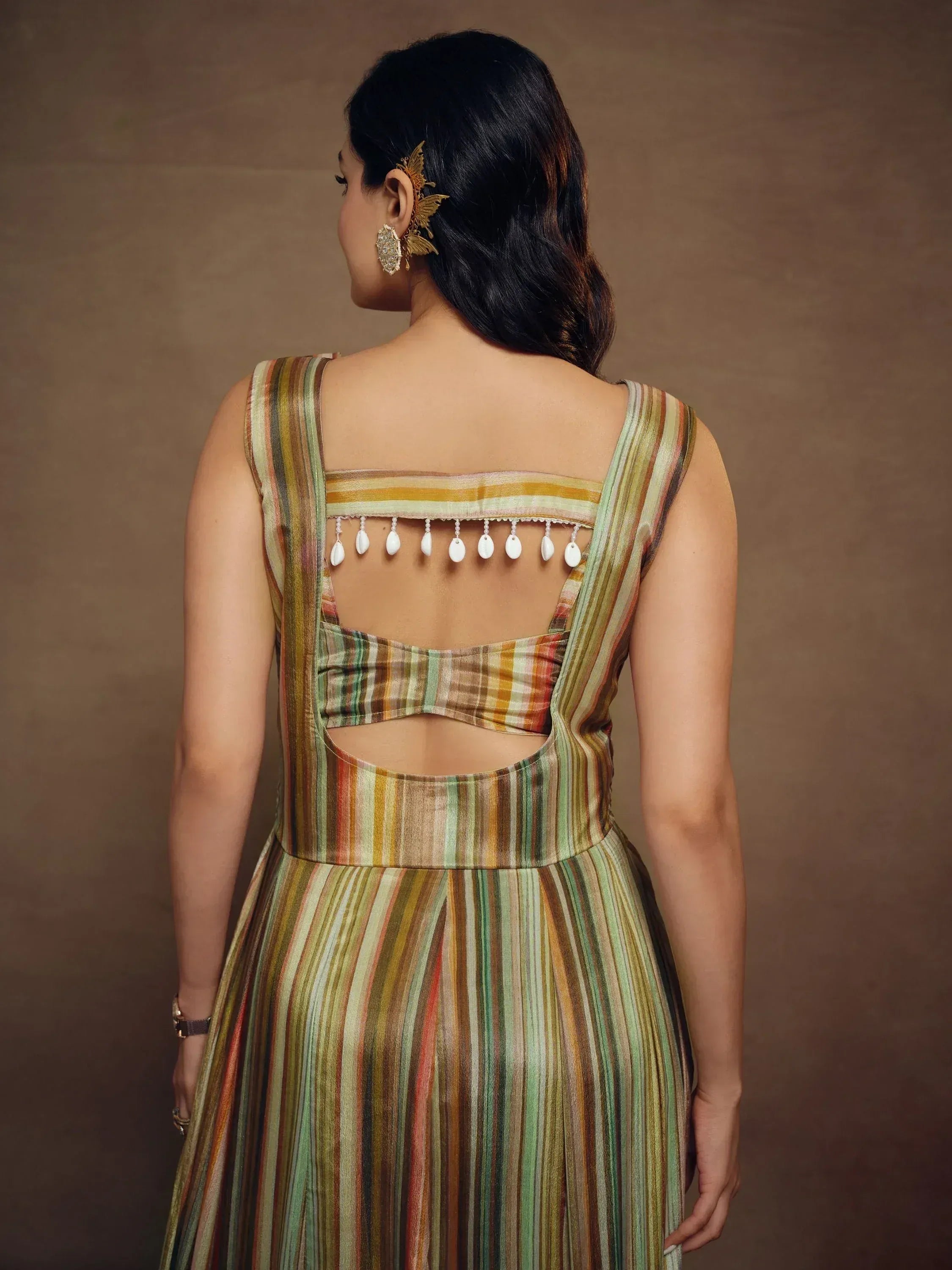 Back view of woman in striped ethnic gown with cutout back and shell tassels, gold hair accessory
