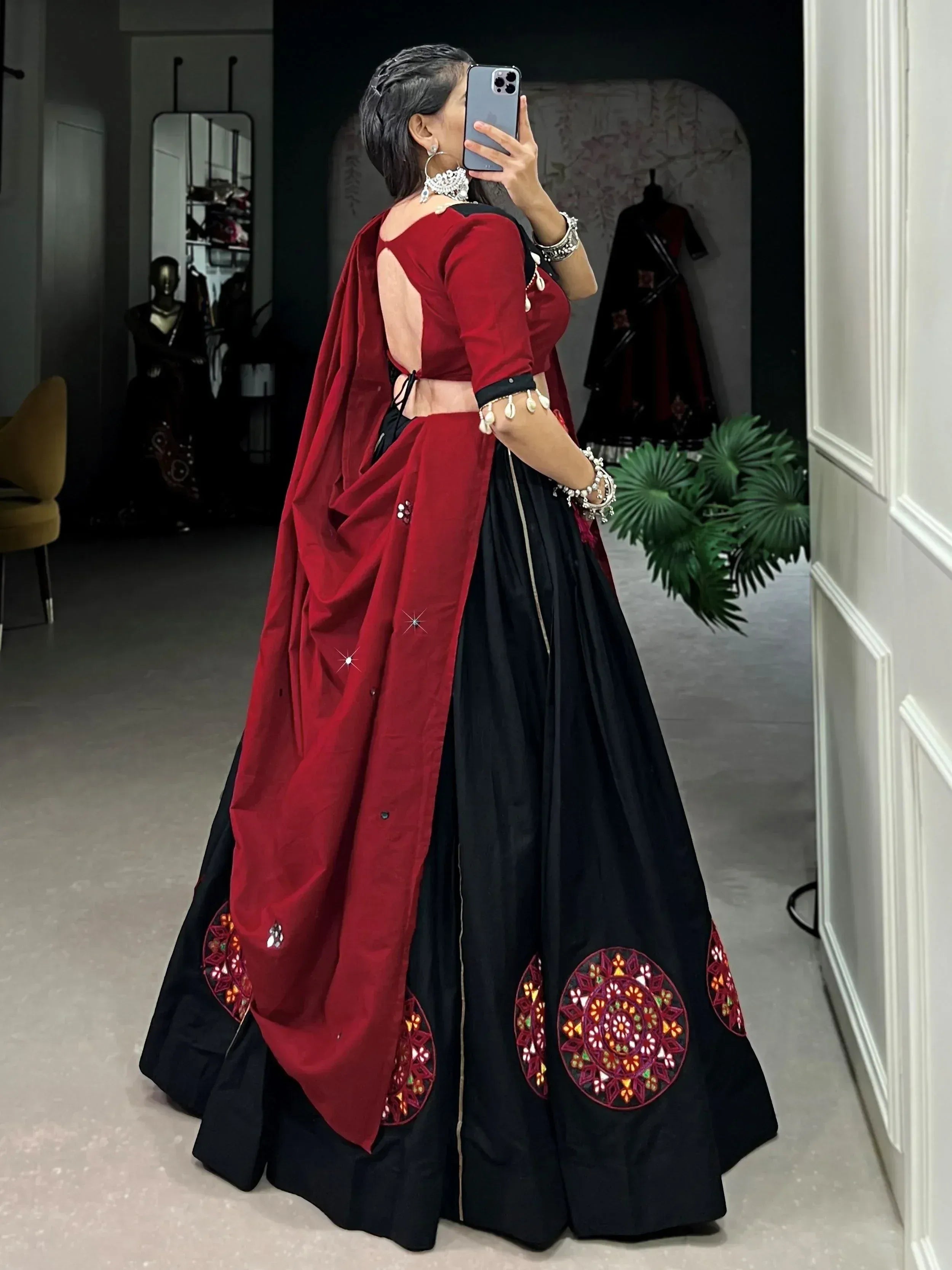 Woman in black and red ethnic lehenga choli with mirror work, taking mirror selfie in boutique