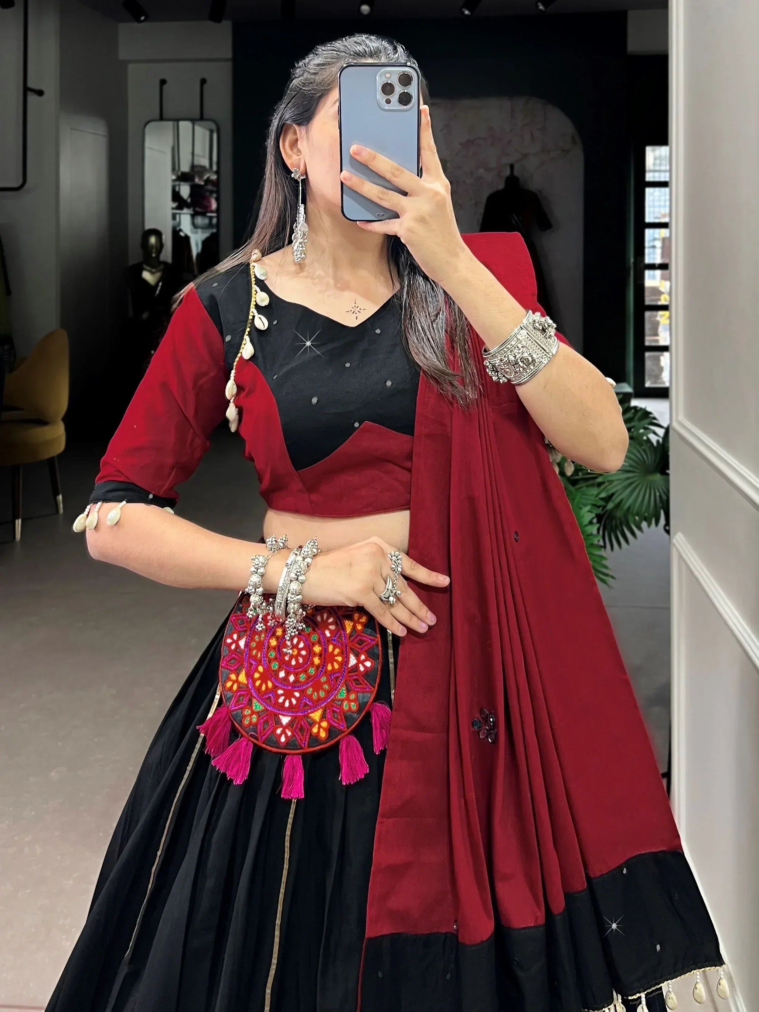 Woman in black and red ethnic lehenga choli with mirror work, shell jewelry, and embroidered potli bag